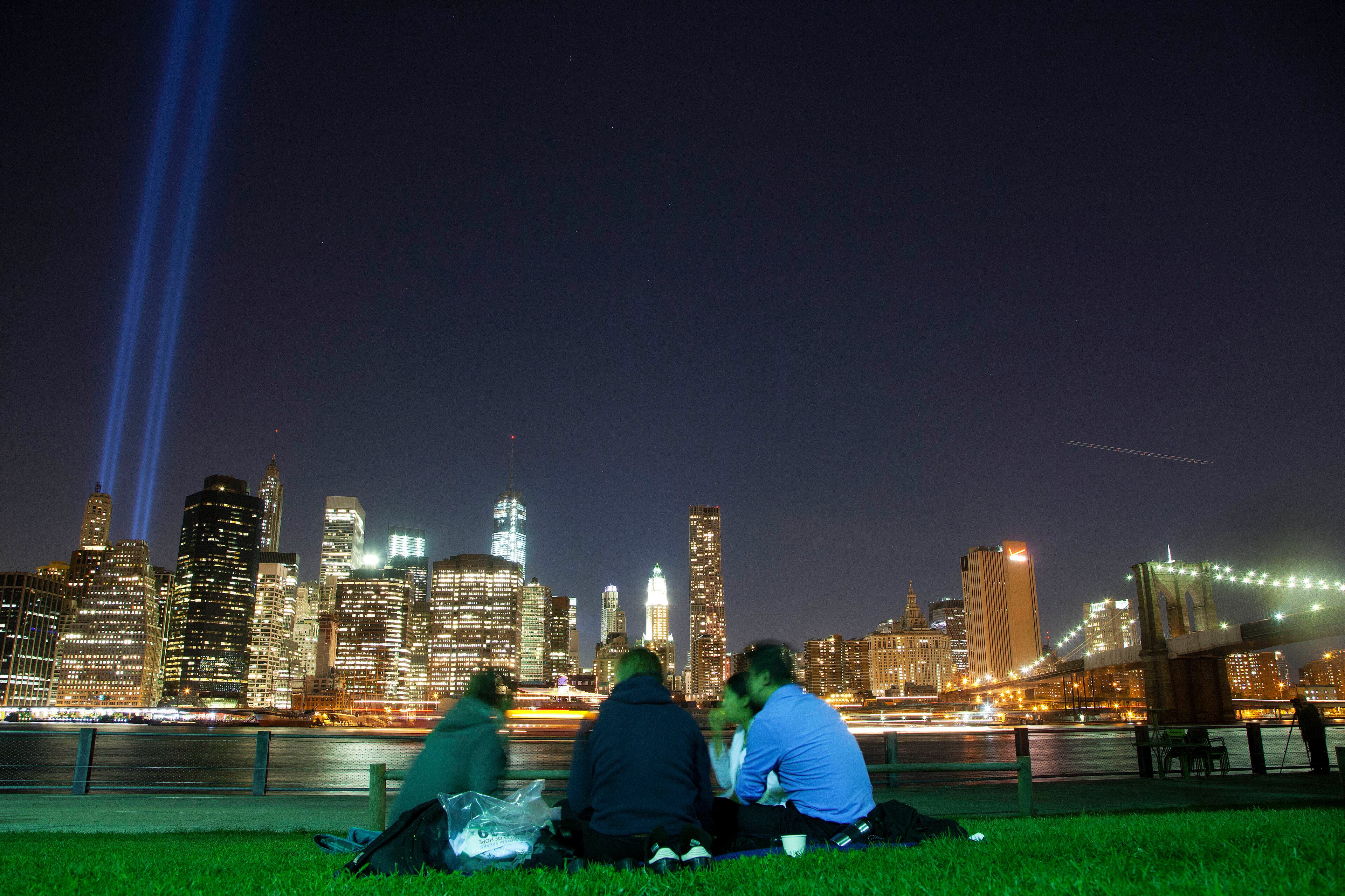 In this Friday, Sept. 7, 2013 photo, people in Brooklyn Bridge Park gather to watch a test of the Tribute in Light rising from the lower Manhattan skyline in New York. The Tribute, which commemorates the fallen twin towers, will be on display, Wednesday, Sept. 11, the 12th anniversary of the terrorist attacks. (AP Photo/Mark Lennihan)