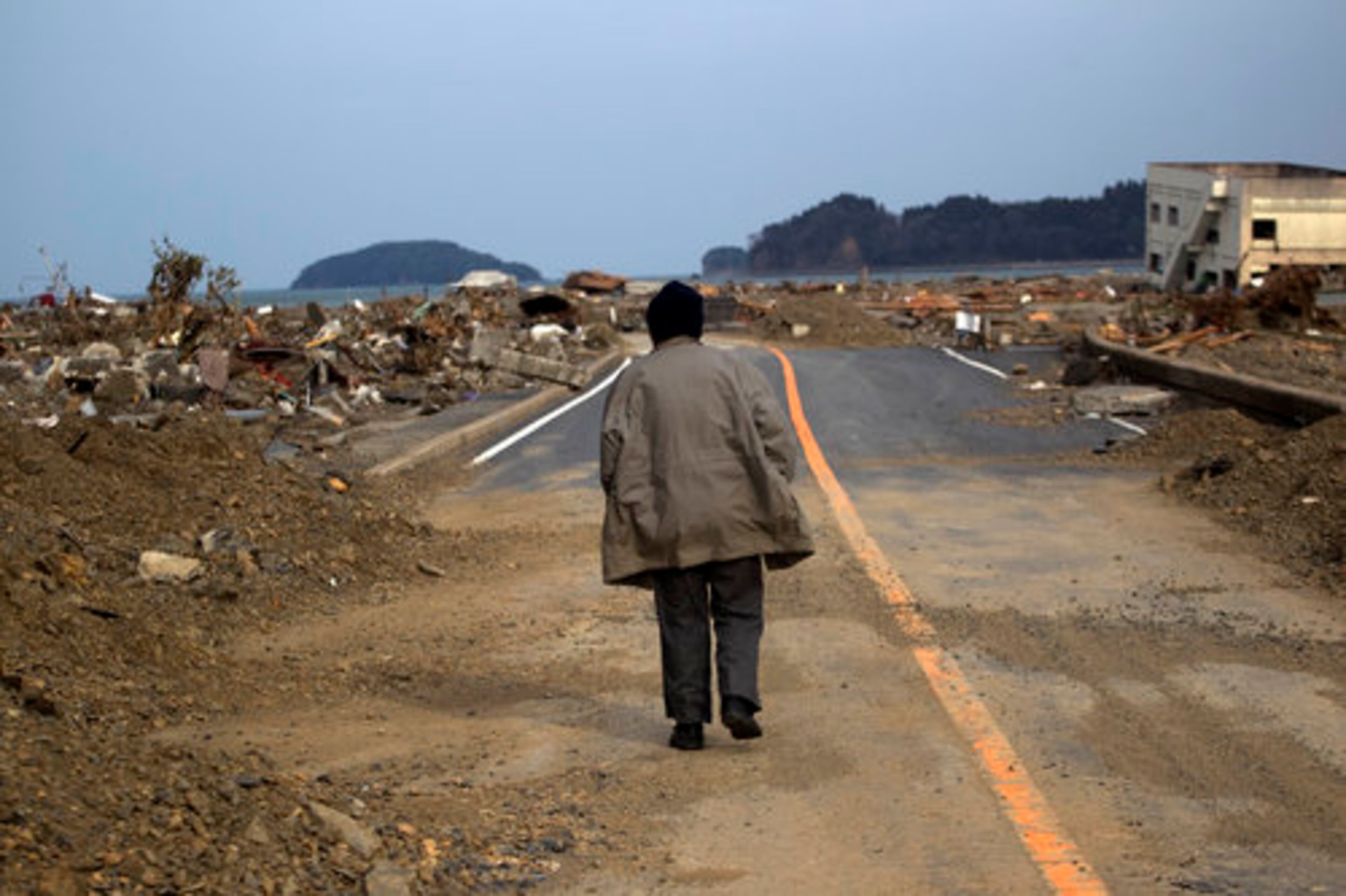 A Japanese earthquake and tsunami survivor walks alone on a road past the destroyed village of Saito, in northeastern Japan, Monday, March 14, 2011.