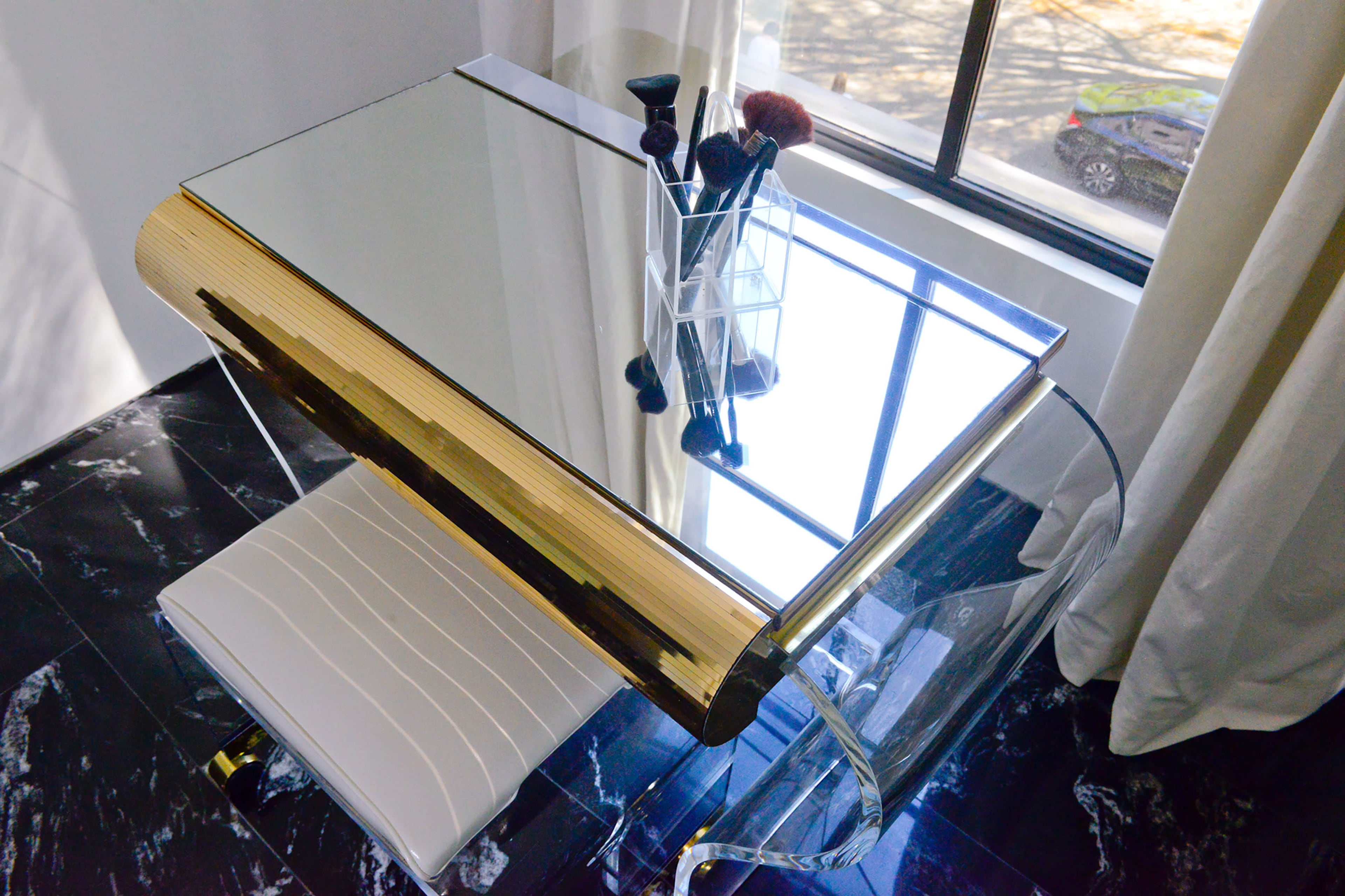 Offset by black tiles on the floor, a vintage Lucite dressing table with a mirrored top and brass accents from Etsy adds a glamorous touch to the master bathroom.