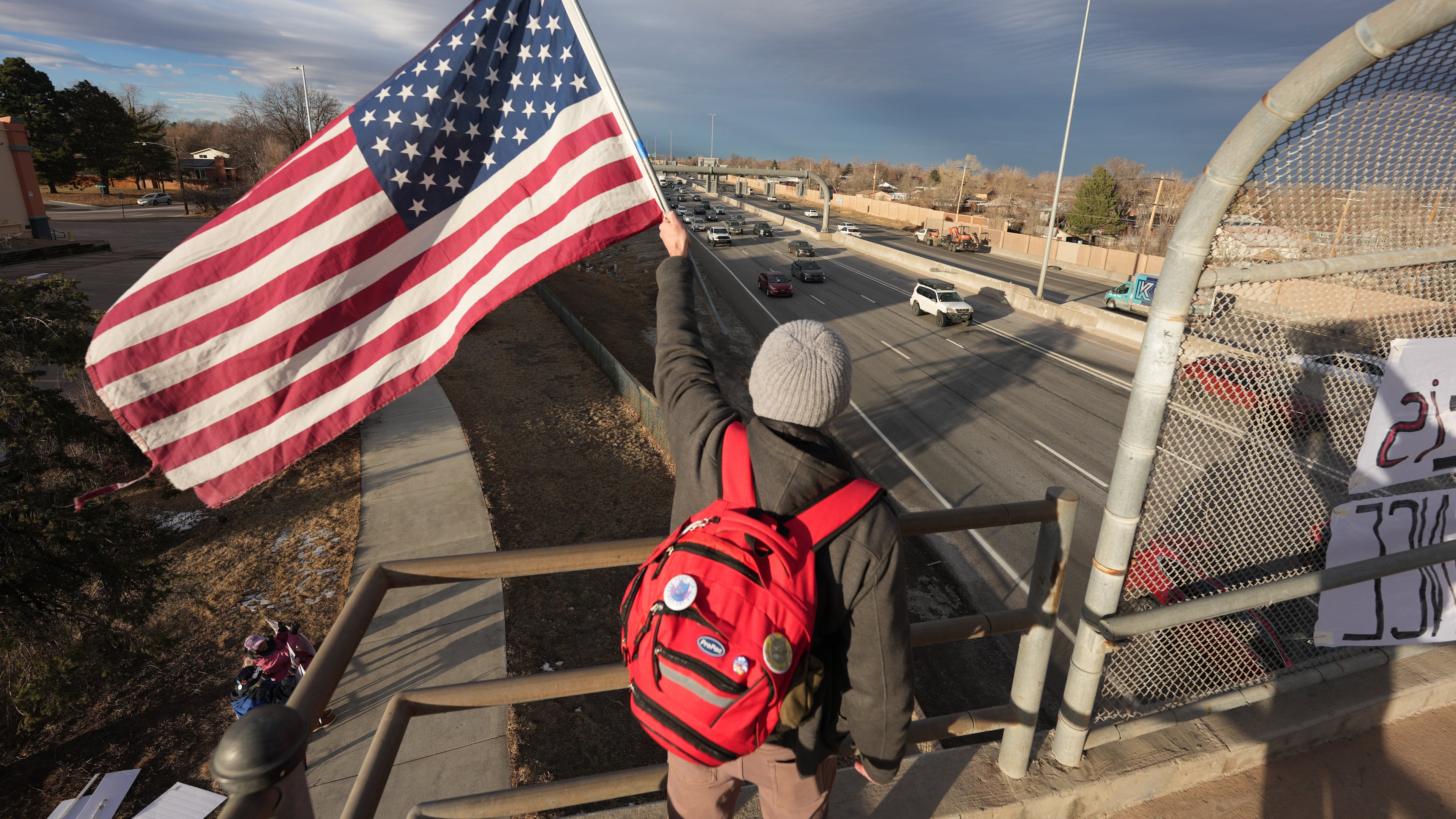 A protester holds American flag while waving at motorists Wednesday, Jan. 28, 2026, from an overpass along Interstate 25 in Northglenn, Colo. (AP Photo/David Zalubowski)