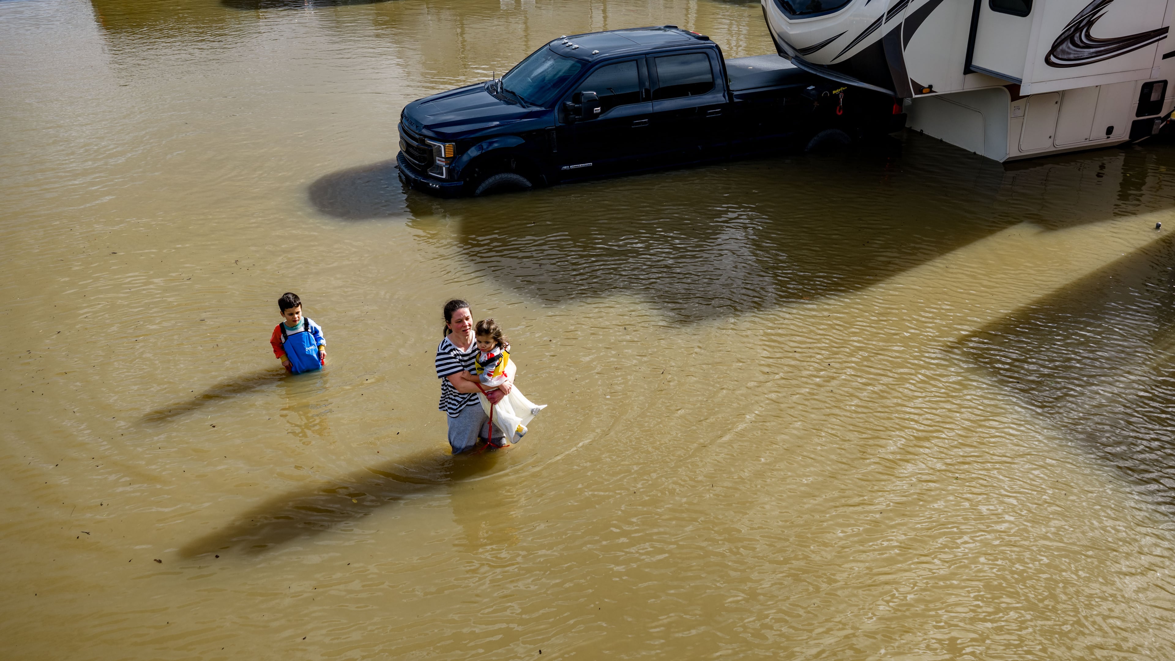 FILE - People wade through a recreational vehicle park flooded by a king tide on Jan. 3, 2026, near Corte Madera in Marin County, Calif. (AP Photo/Ethan Swope, File)