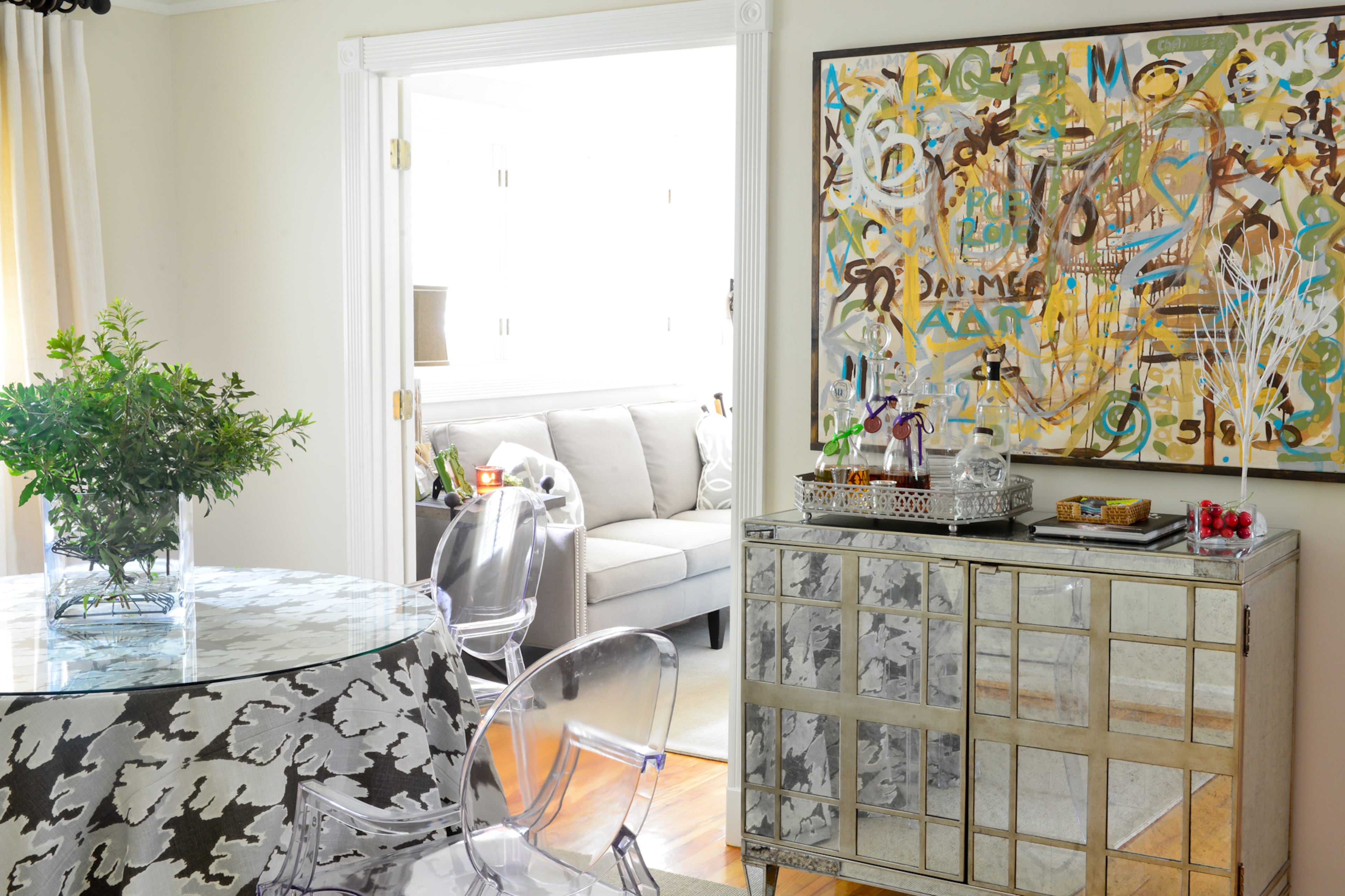 Creating the dining table was a family affair. Betsy Clay's mother found the table at a dumpster, and her husband's grandfather built the round topper and drilled it into the existing table, to increase the tabletop. Kelly Wearstler's "Bengal Bazaar" fabric in an organic design is placed underneath a glass top, and acrylic chairs surround the table.