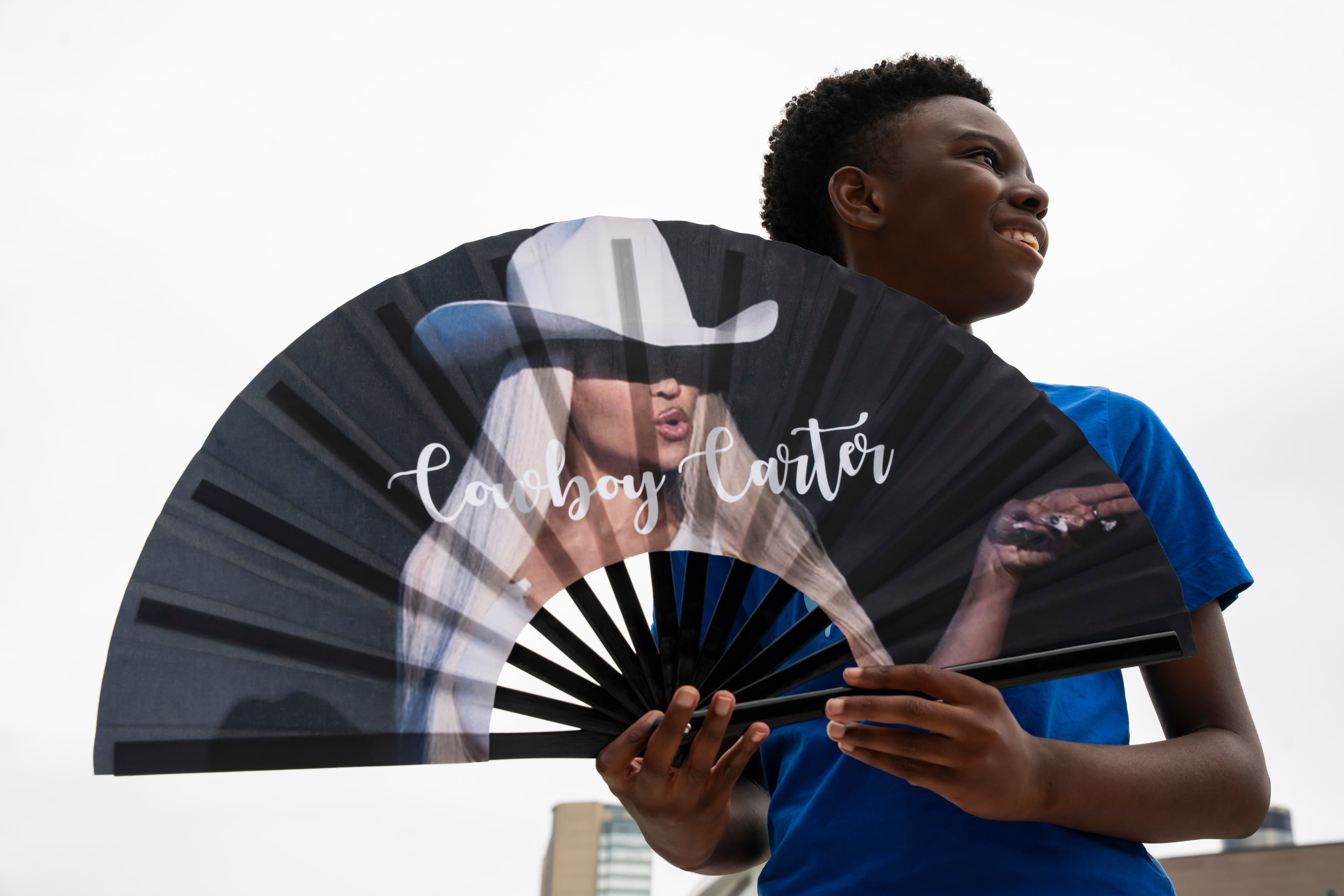 A boy selling Beyoncé merch holds out a fan in line outside Beyonce's Cowboy Carter concert in Atlanta on Thursday, July 10, 2025. (Olivia Bowdoin for the AJC)