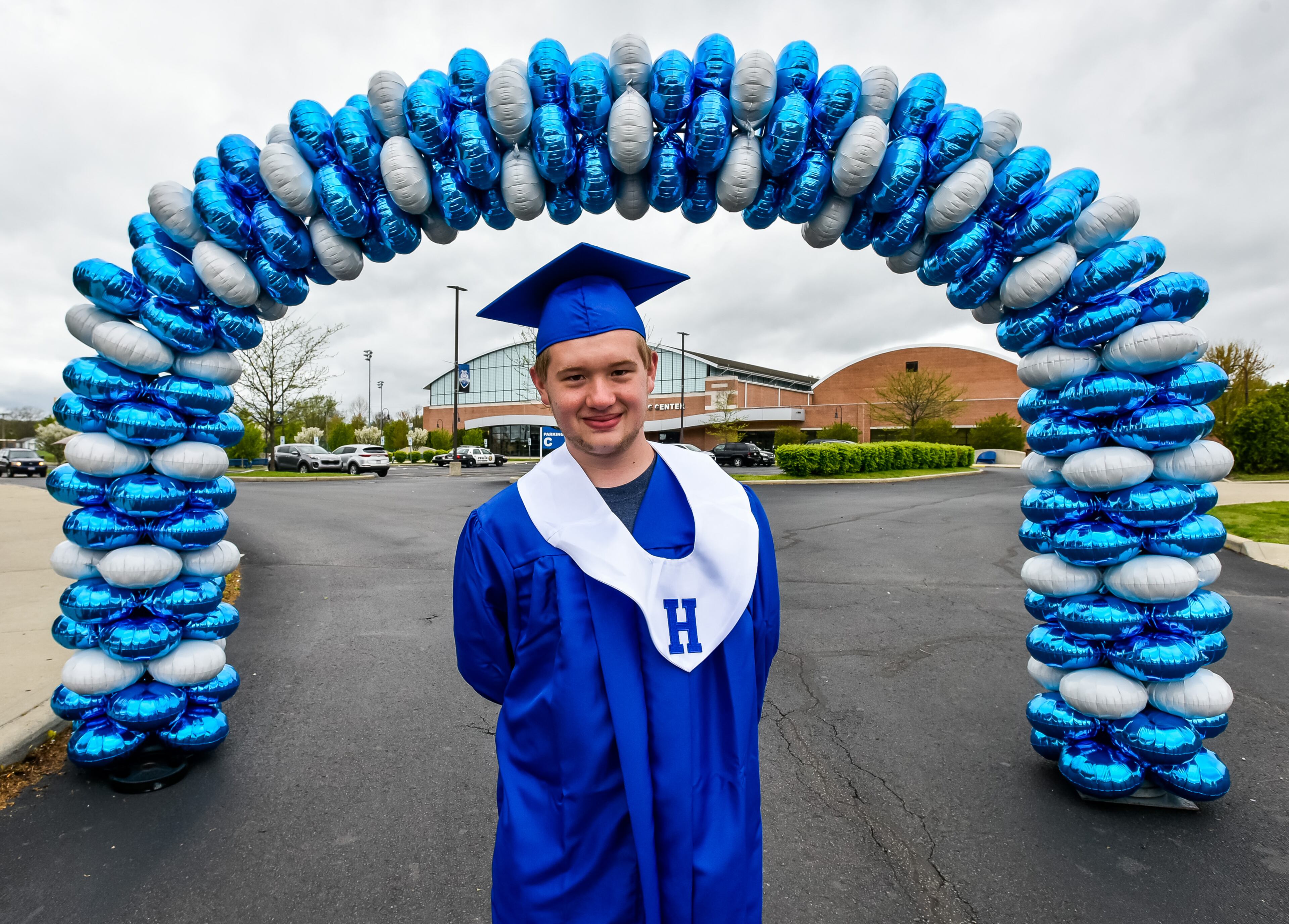 Senior Danny Marlar stands for a photo under a balloon arch under his mom's directon as Hamilton High School seniors picked up their caps and gowns Thursday, April 30, 2020 at Hamilton High School in Hamilton. The seniors and parents were greeted by signs drove through balloon arches as they picked up their graduation supplies in drive-thru fashion. Schools around the area are still trying to figure out how to make graduations ceremonies special for students while keeping with the social distancing guidelines. Hamilton has not announced their plans yet for graduation. NICK GRAHAM / STAFF