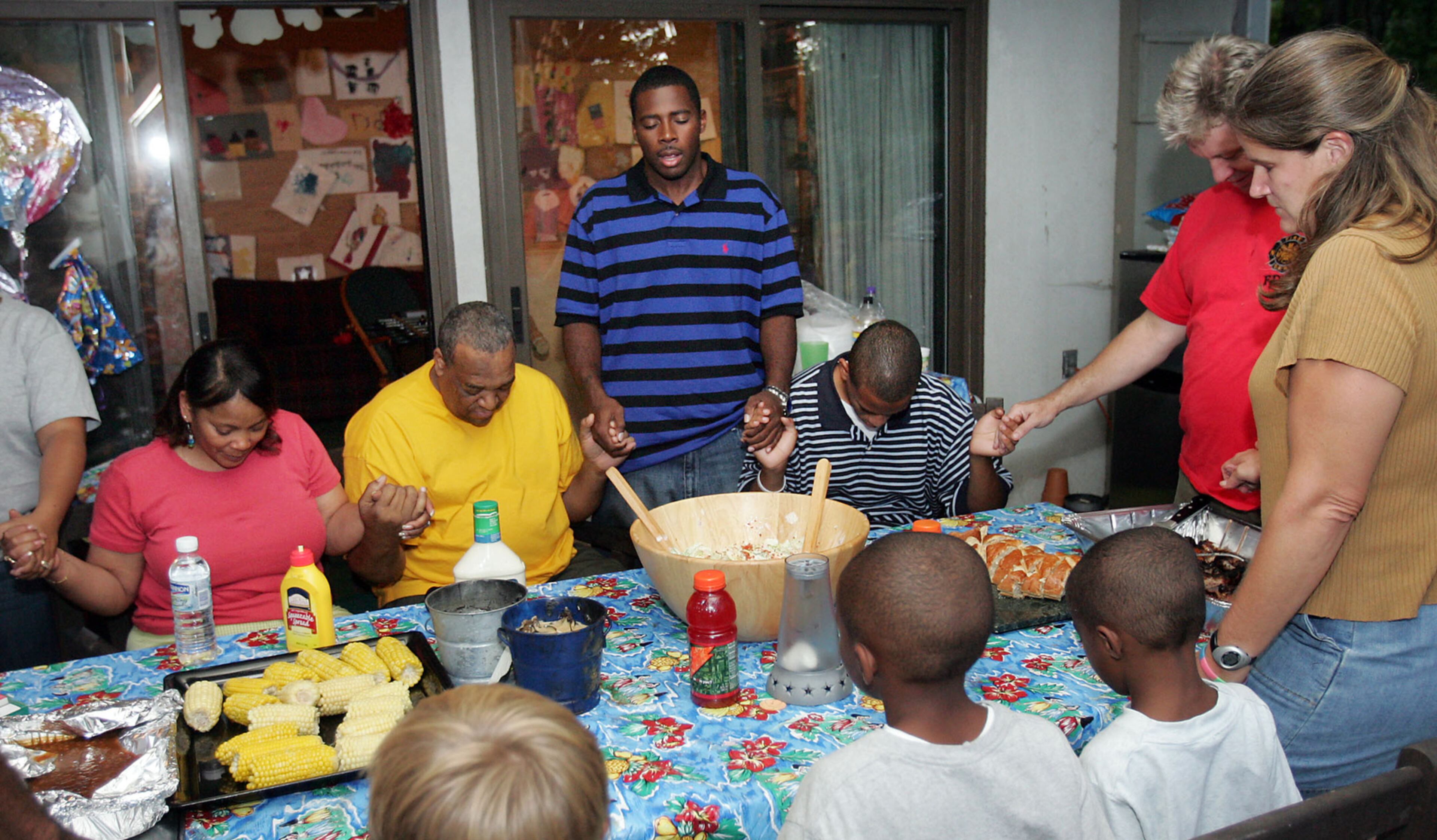 050908- Myron Celestine (standing) says grace before dinner. At left are Sylvia and Charles Cook. To the right of Myron are Richean Cook and Boake and Carol Moore. Carol and Boake Moore of Roswell have 4 children and a house in Roswell and have taken in a group of evacuees from New Orleans. The children from these two different cultures are growing close, and the adults are too. BOB ANDRES/STAFF