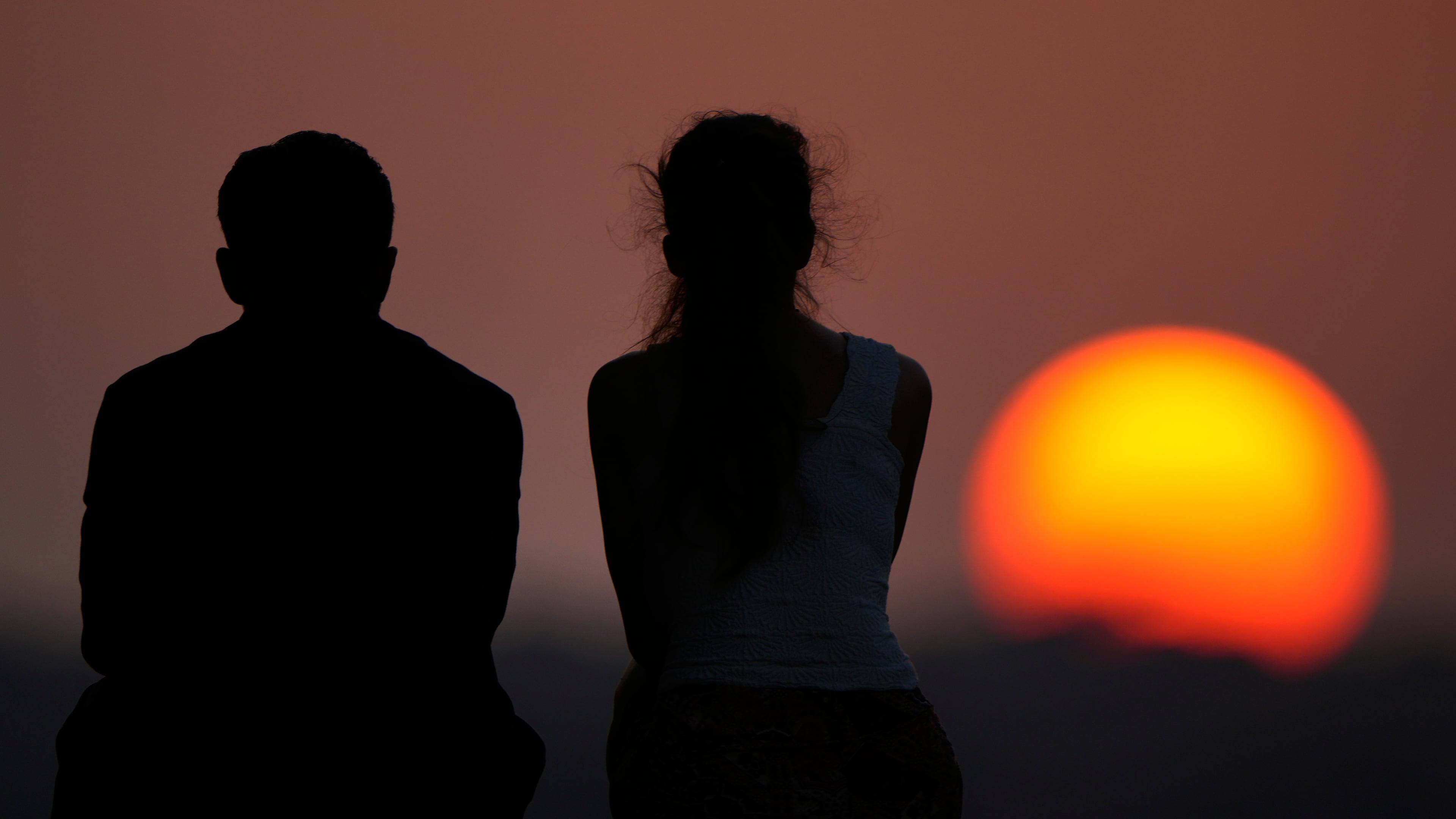 People watch the setting sun at the end of a hot summer day, Sunday, July 26, 2026, in Kansas City, Mo. (AP Photo/Charlie Riedel)