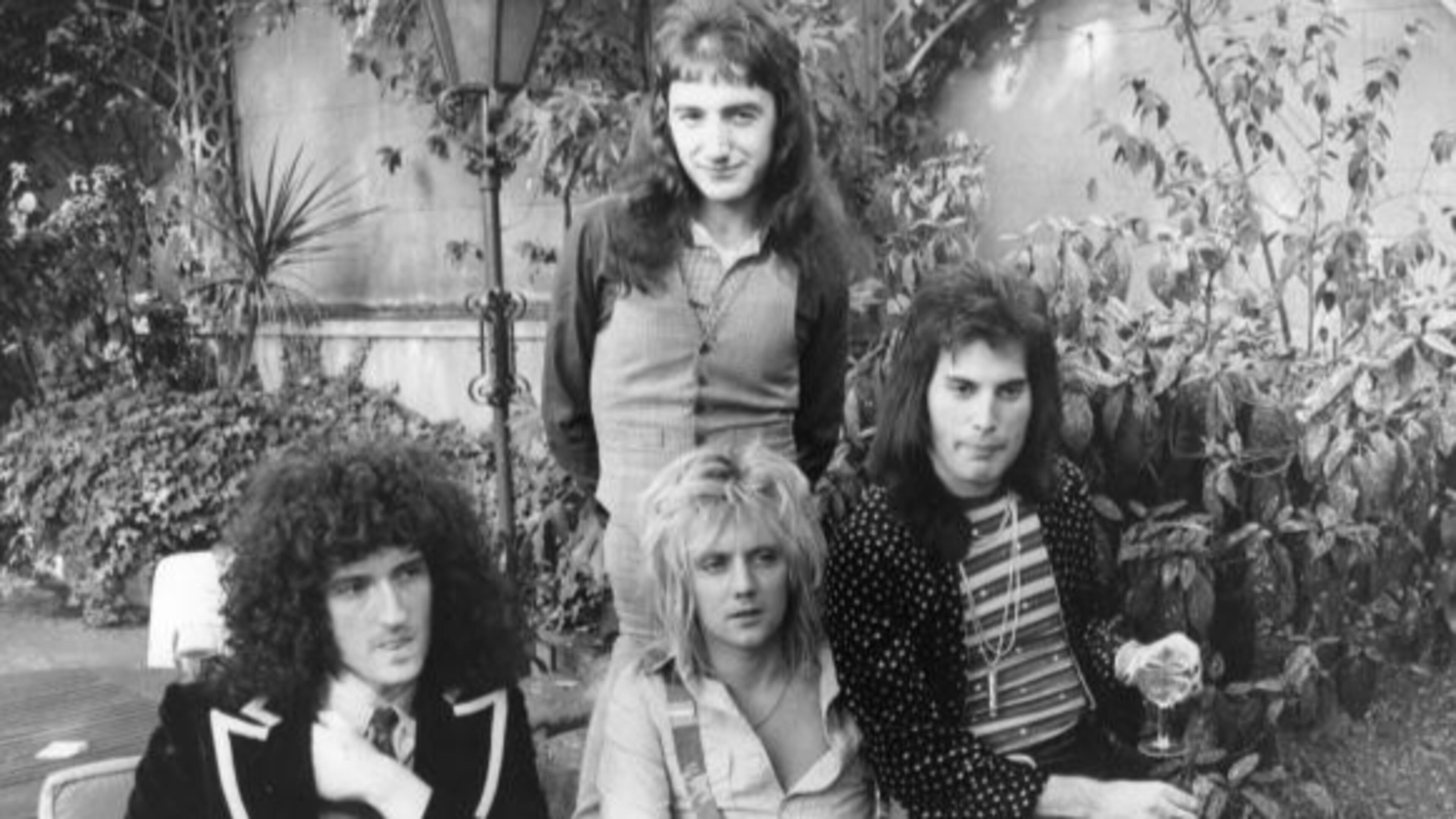 September 1976: British rock group Queen at Les Ambassadeurs, where they were presented with silver, gold and platinum discs for sales in excess of one million of their hit single 'Bohemian Rhapsody', which was No 1 for 9 weeks. The band are, from left to right; Brian May, John Deacon (standing), Roger Taylor and Freddie Mercury (Frederick Bulsara, 1946 - 1991). (Photo by Ian Tyas/Keystone/Getty Images)