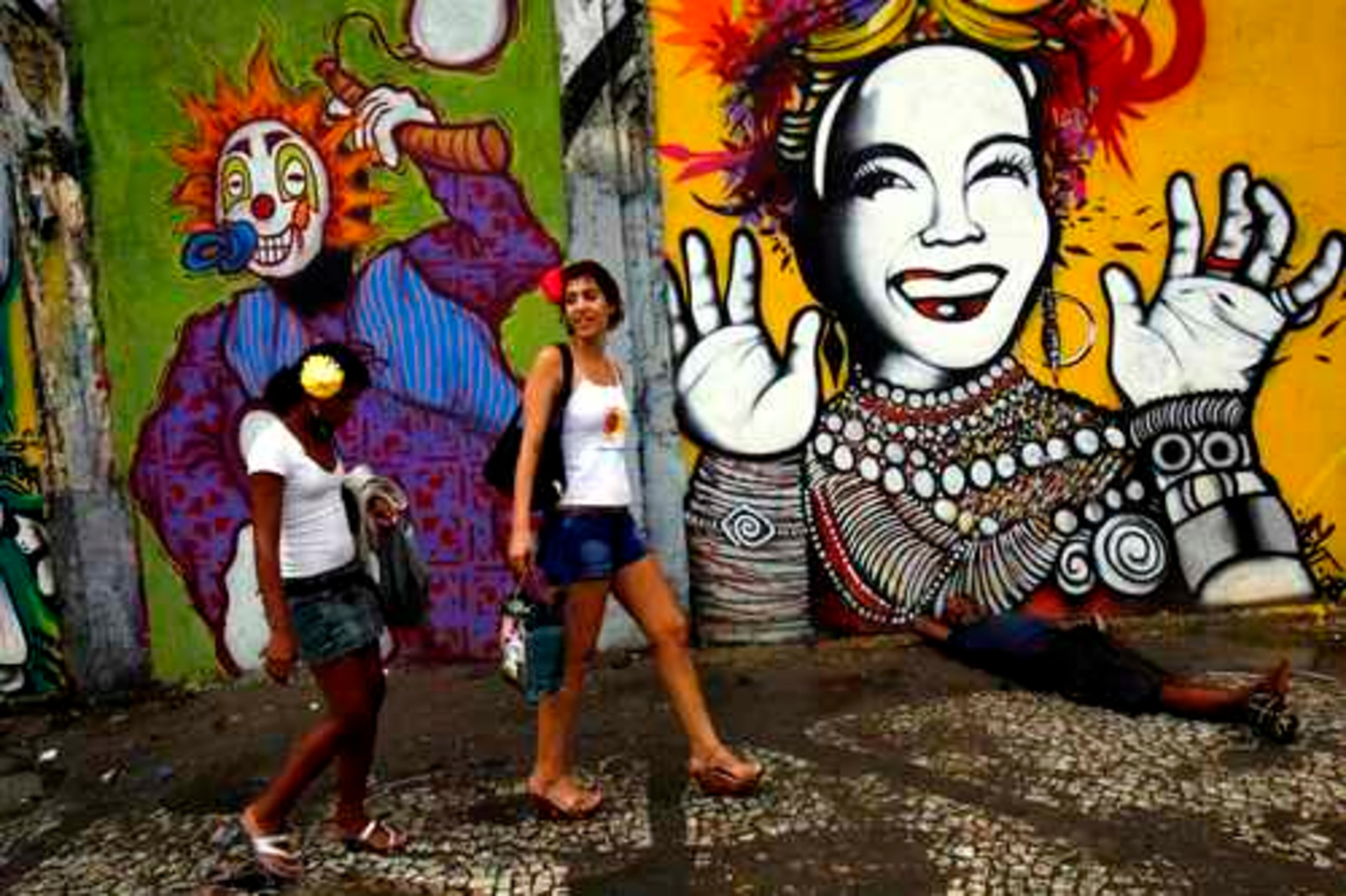 Revelers make their way back home as a man sleeps by the floor in front a graffiti-covered wall with carnival characters in Rio de Janeiro.