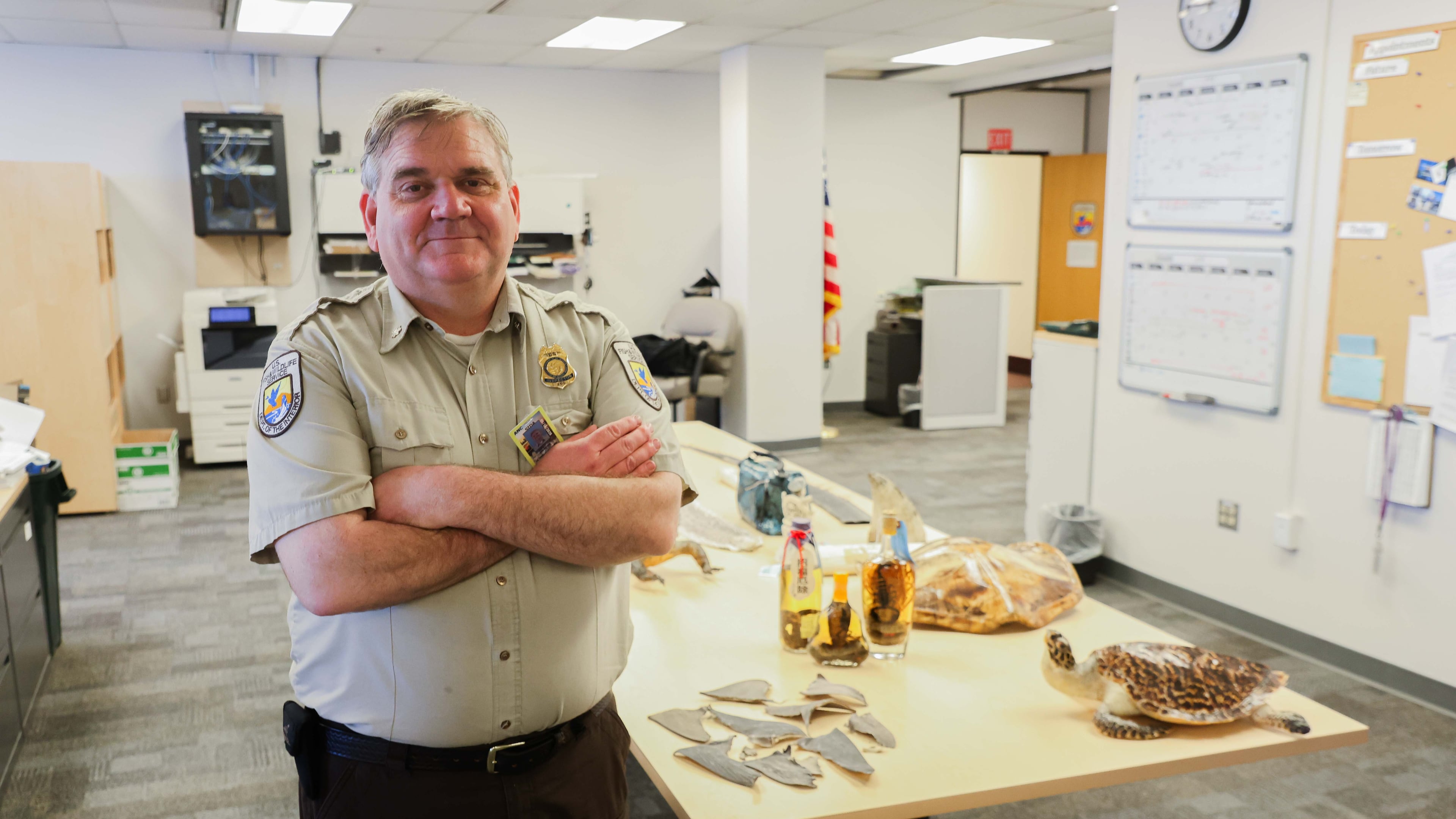 Chris Andrews poses for a photo with confiscated goods, June 4, 2026, at his office in the Ted Stevens Anchorage International Airport in Anchorage, Ala. (James Daggett/Alaska Public Media via AP)