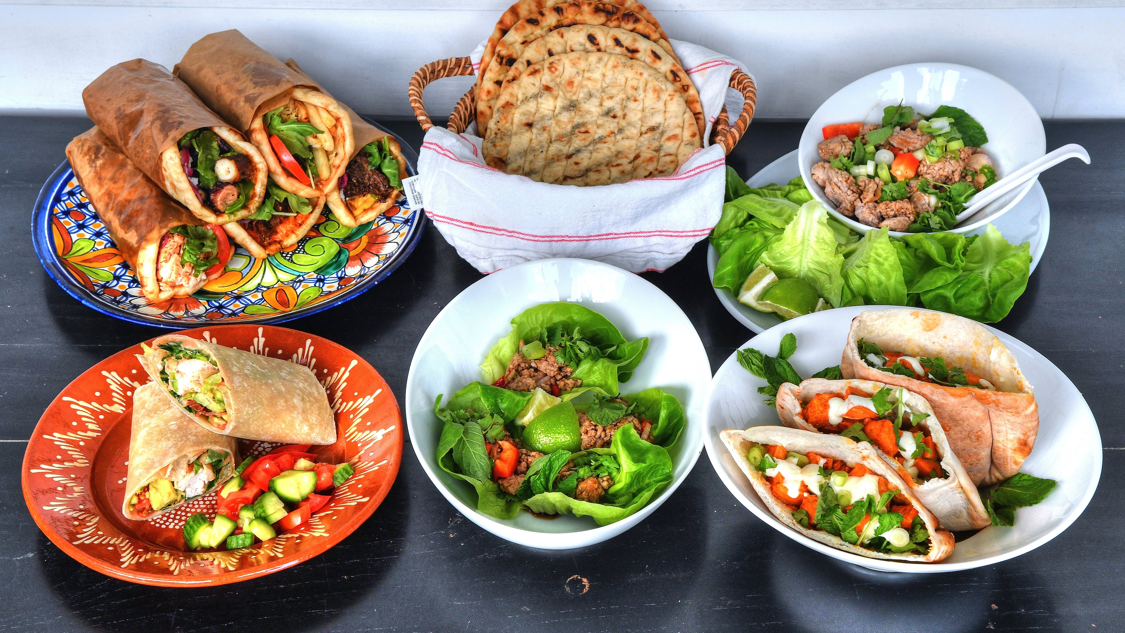 Hand-held meals that will tempt you include (top row, from left) assorted pita wraps from Kyma executive chef Pano Karatassos' Lamb Shack, Homemade Pita Bread (a recipe from Karatassos' cookbook), a DIY setup for Laotian Larb Lettuce Wraps; and (bottom row, from left) Poco Loco chef's Grilled Chicken BLT Burrito With BBQ Crema, Laotian Larb Lettuce Wraps and Yalla executive chef Todd Ginsberg's Roasted Sweet Potato Pockets With Whipped Feta Dressing. Styling by Lisa Hanson / Chris Hunt for the AJC