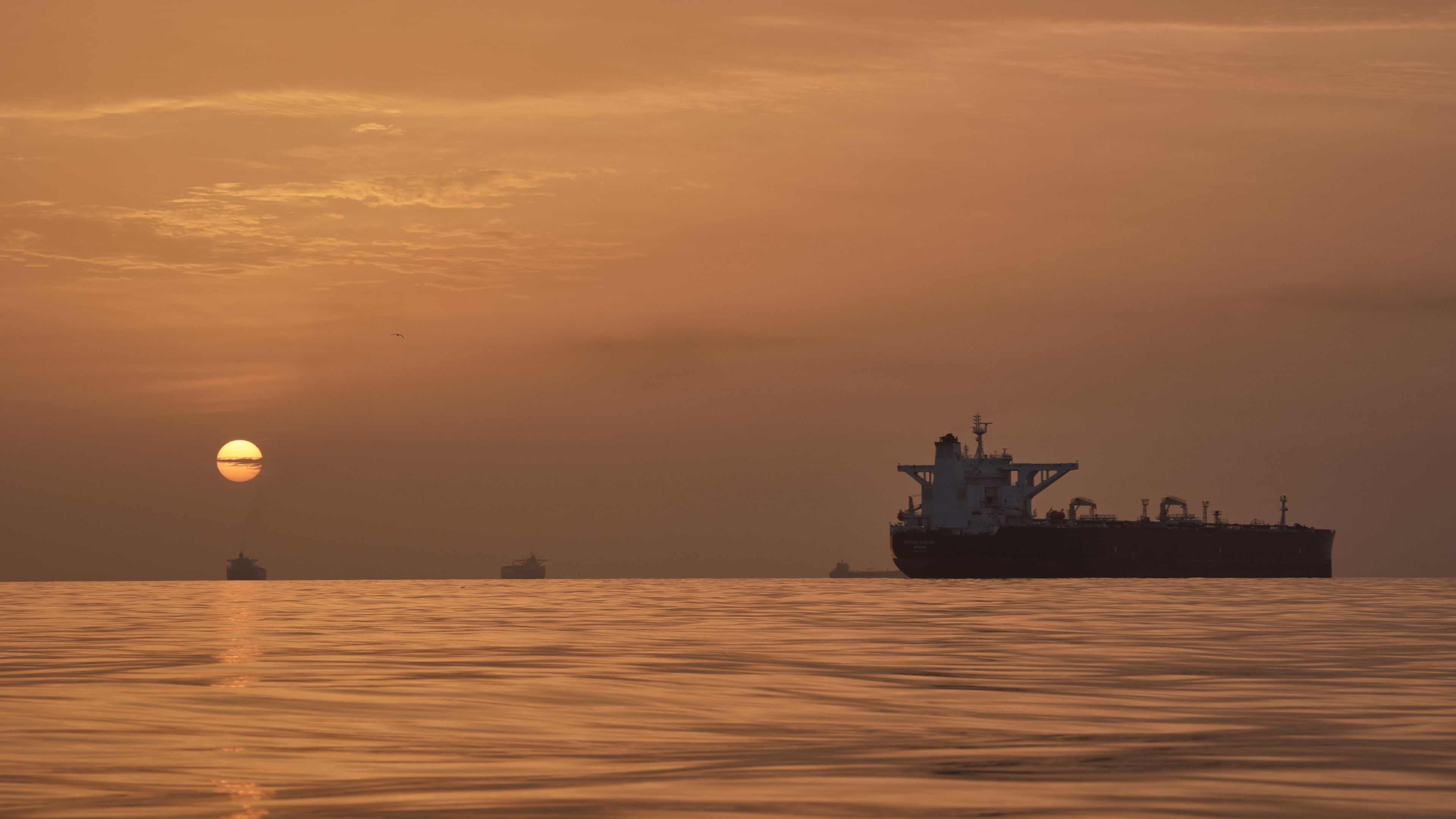 The sun rises behind tankers anchored in the Strait of Hormuz off the coast of Qeshm Island, Iran, Saturday, April 18, 2026. (AP Photo/Asghar Besharati)