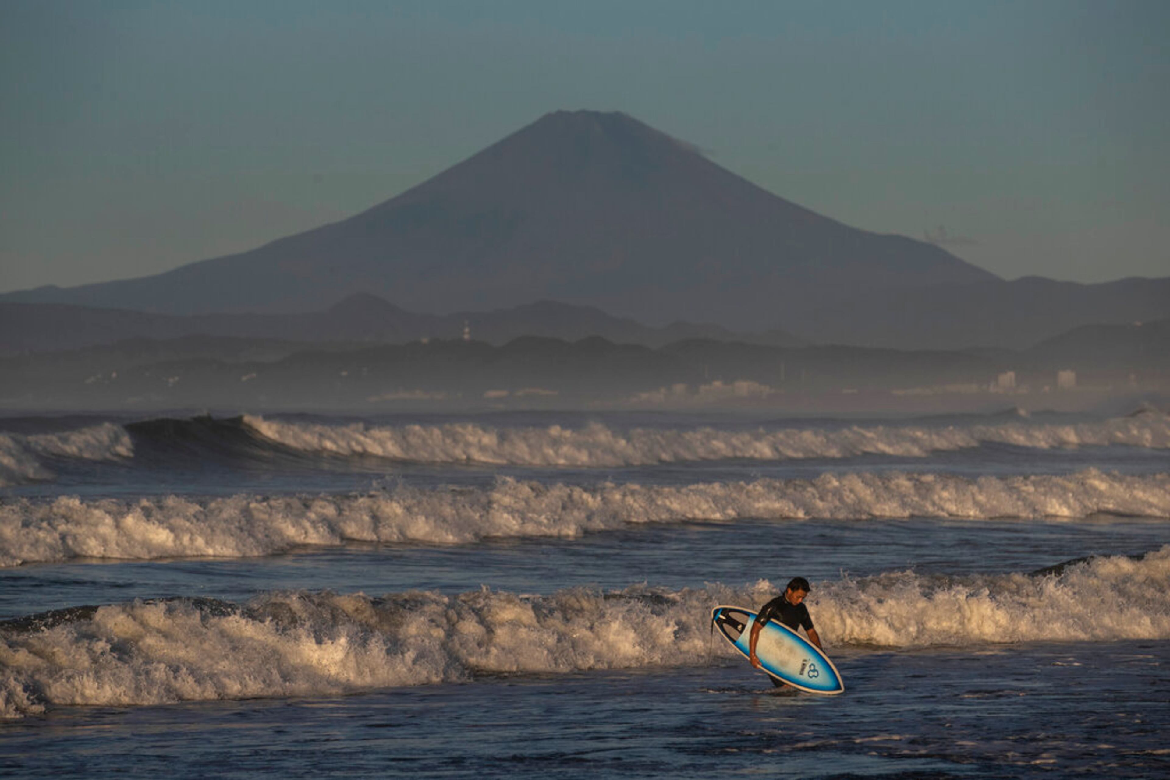 A surfer walks out of the water as Mount Fuji is visible in the distance after Typhoon Hagibis passed through the area, Sunday, Oct. 13, 2019, in Fujisawa, west of Tokyo. A heavy downpour and strong winds pounded Tokyo and surrounding areas on Saturday as a powerful typhoon forecast to be Japan's worst in six decades made landfall and passed over the capital, where streets, nearby beaches and train stations were long deserted. (AP Photo/Jae C. Hong)