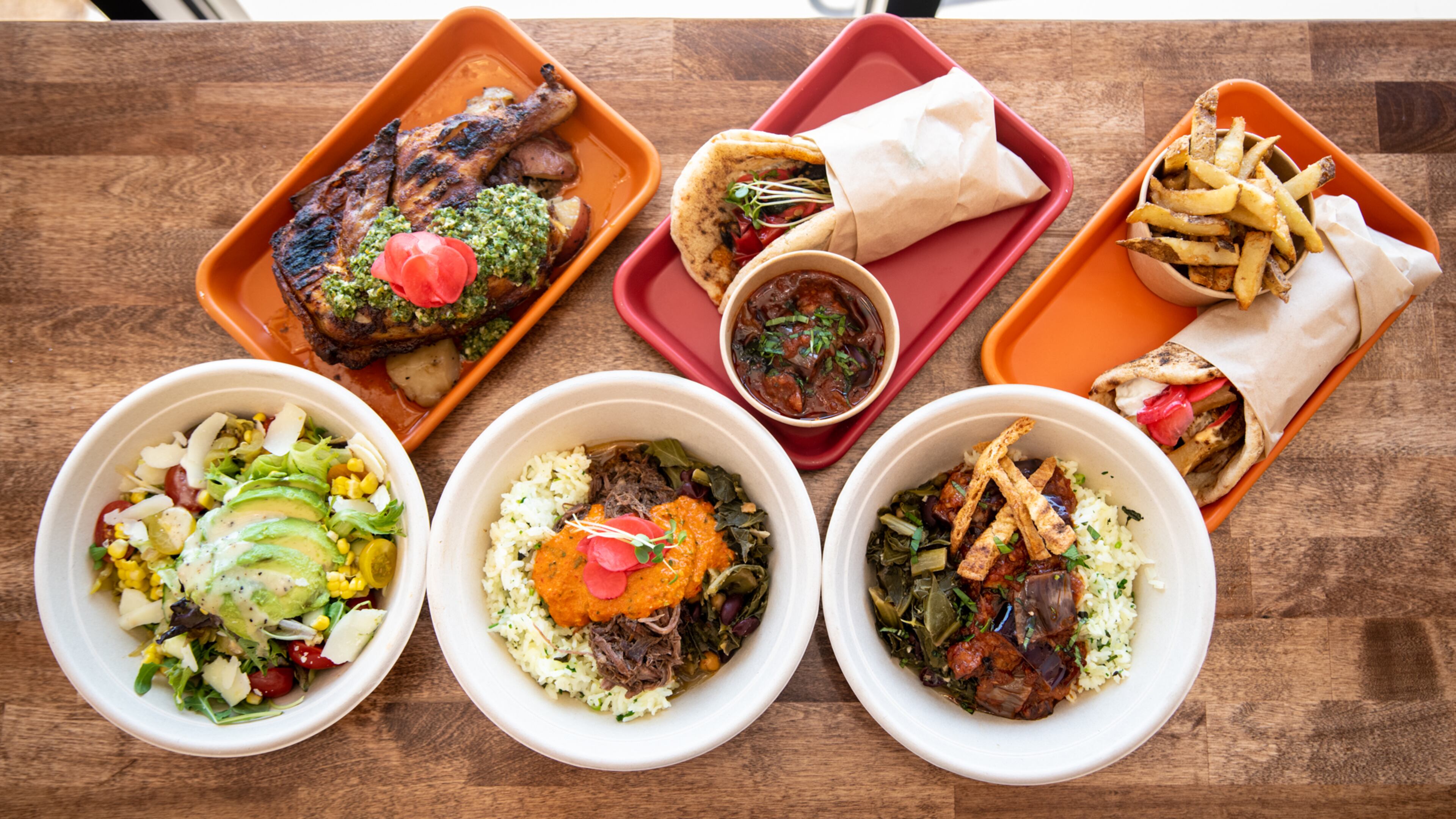 Selections from Karv Kitchen include (top row, from left) Half Rotisserie Chicken, Horta Wrap, Greko Wrap, (bottom row, from left) Corn Avocado Salad, Braised Collard Bowl, and Veggie Collard Bowl. Mia Yakel for The AJC