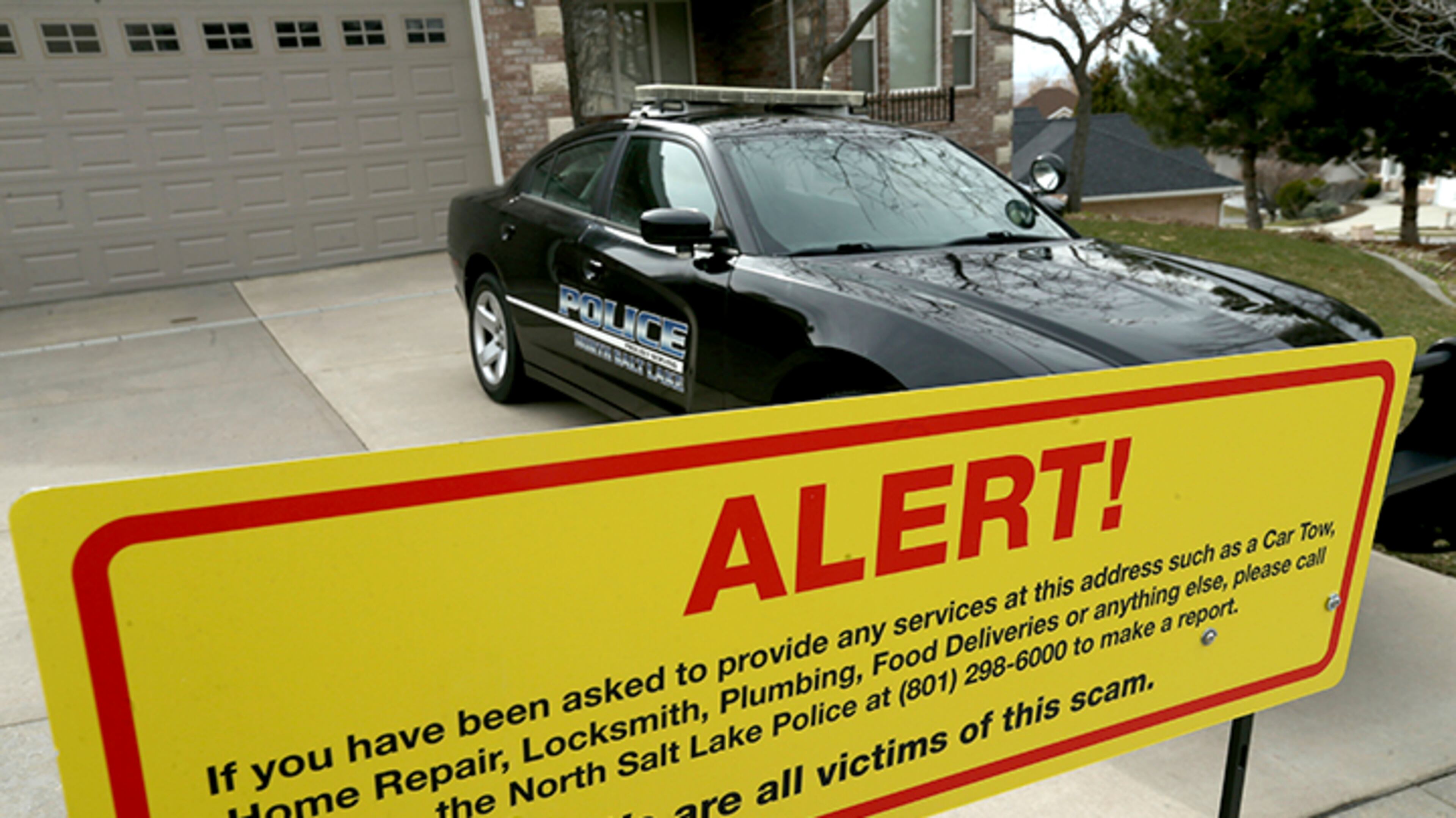 This March 21, 2019 file photo shows a warning sign and a police officer's vehicle at Walt Gilmore's home in North Salt Lake, Utah. U.S. prosecutors arrested Loren Okamura, a Hawaii man, on Nov. 22, who they accuse of sending hundreds of unwanted service providers to the Utah home, including plumbers and prostitutes. It's unknown why the Gilmores were targeted or what if any relationship exists between Okamura and the family.