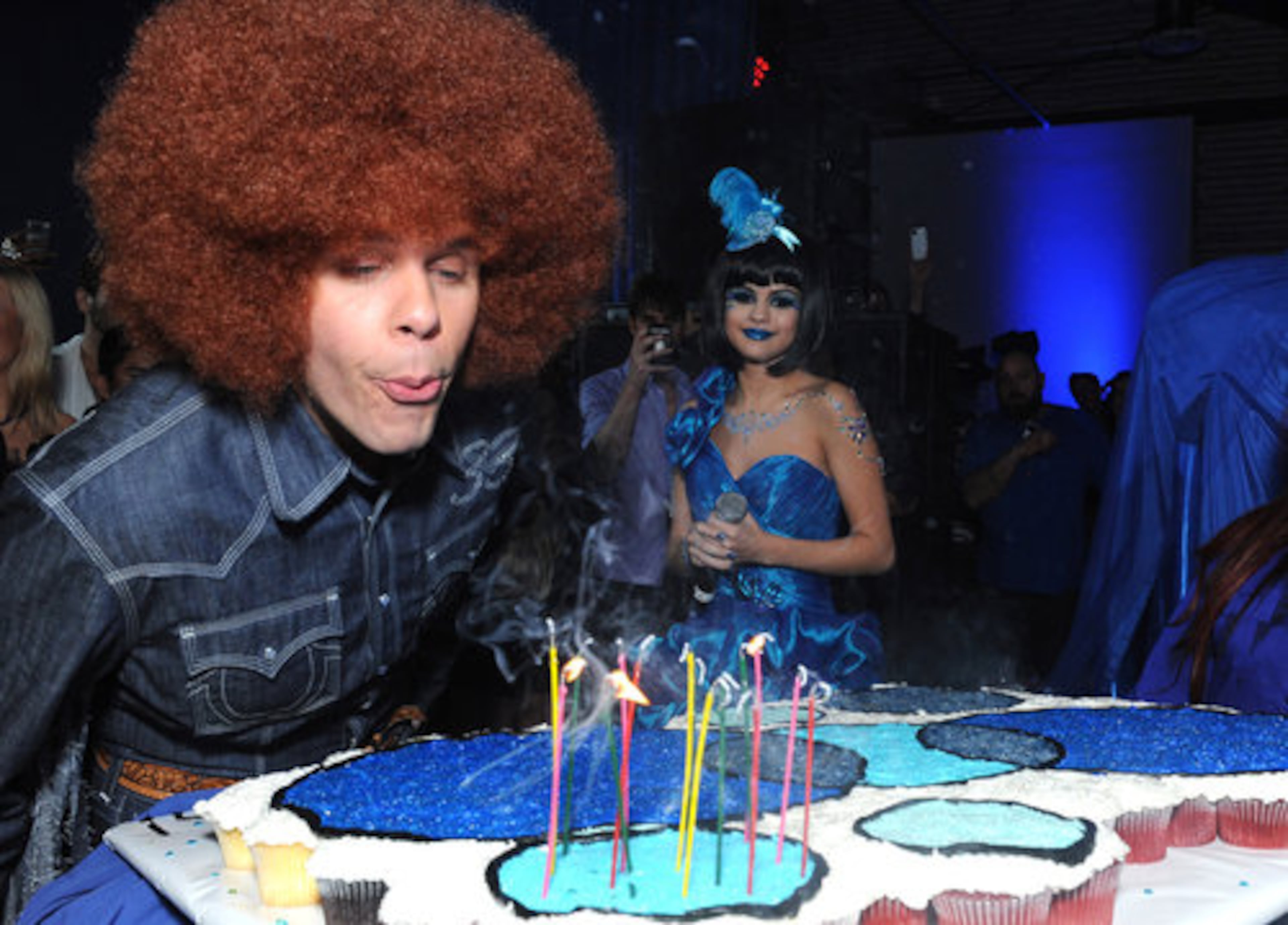 Perez Hilton blows out the candles on his birthday cake during his Blue Ball birthday celebration. In the background is Selena Gomez.