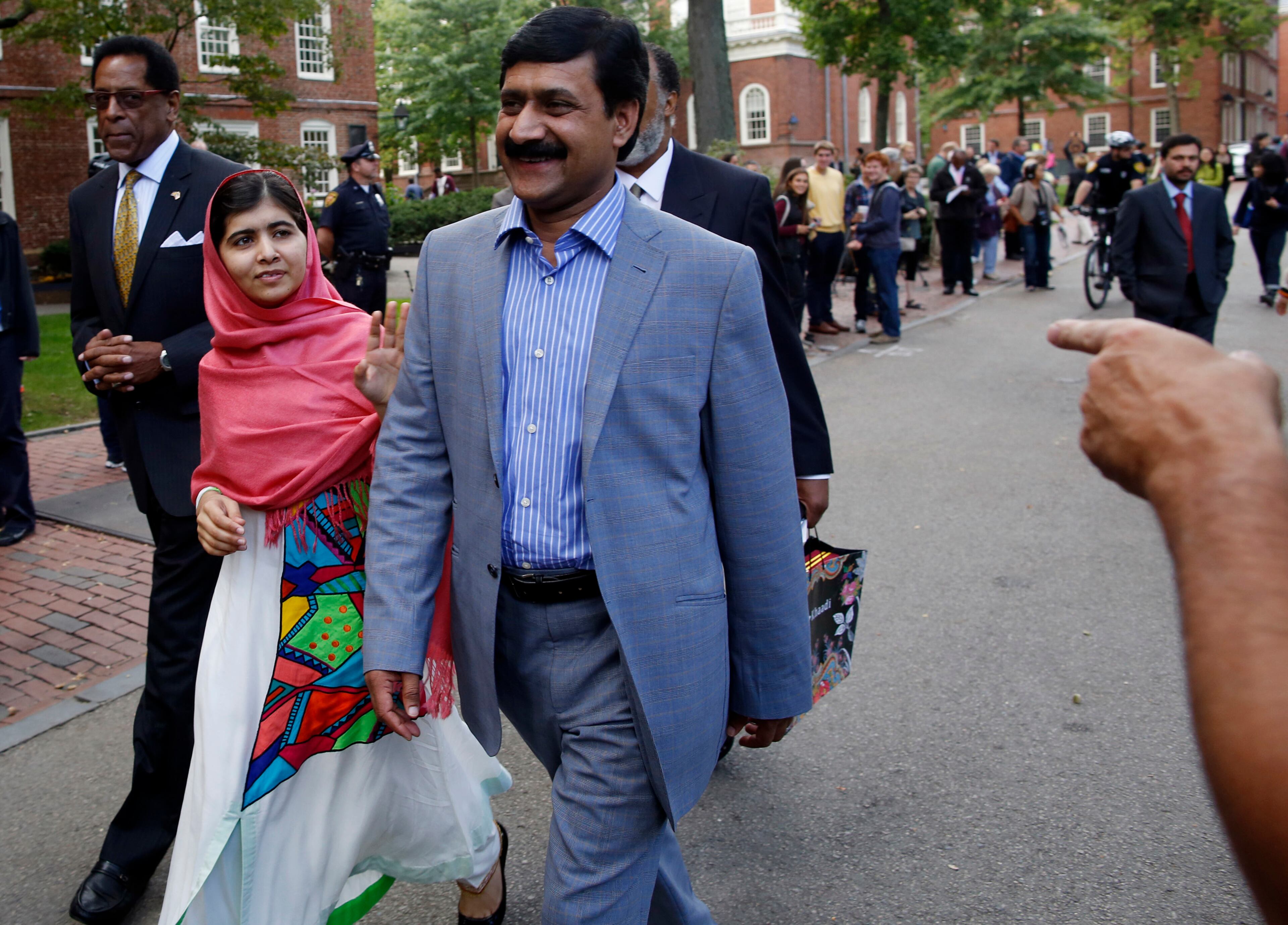 Malala Yousafzai waves to onlookers as she walks with her father, Ziauddin Yousafzai, right, and Director of the Harvard Foundation and Professor of Neurology at Harvard Medical School Dr. S. Allen Counter, through Harvard Yard after a news conference on the campus in Cambridge, Mass. on Friday, Sept. 27, 2013. The Pakistani teenager, an advocate for education for girls, survived a Taliban assassination attempt in 2012 on her way home from school.