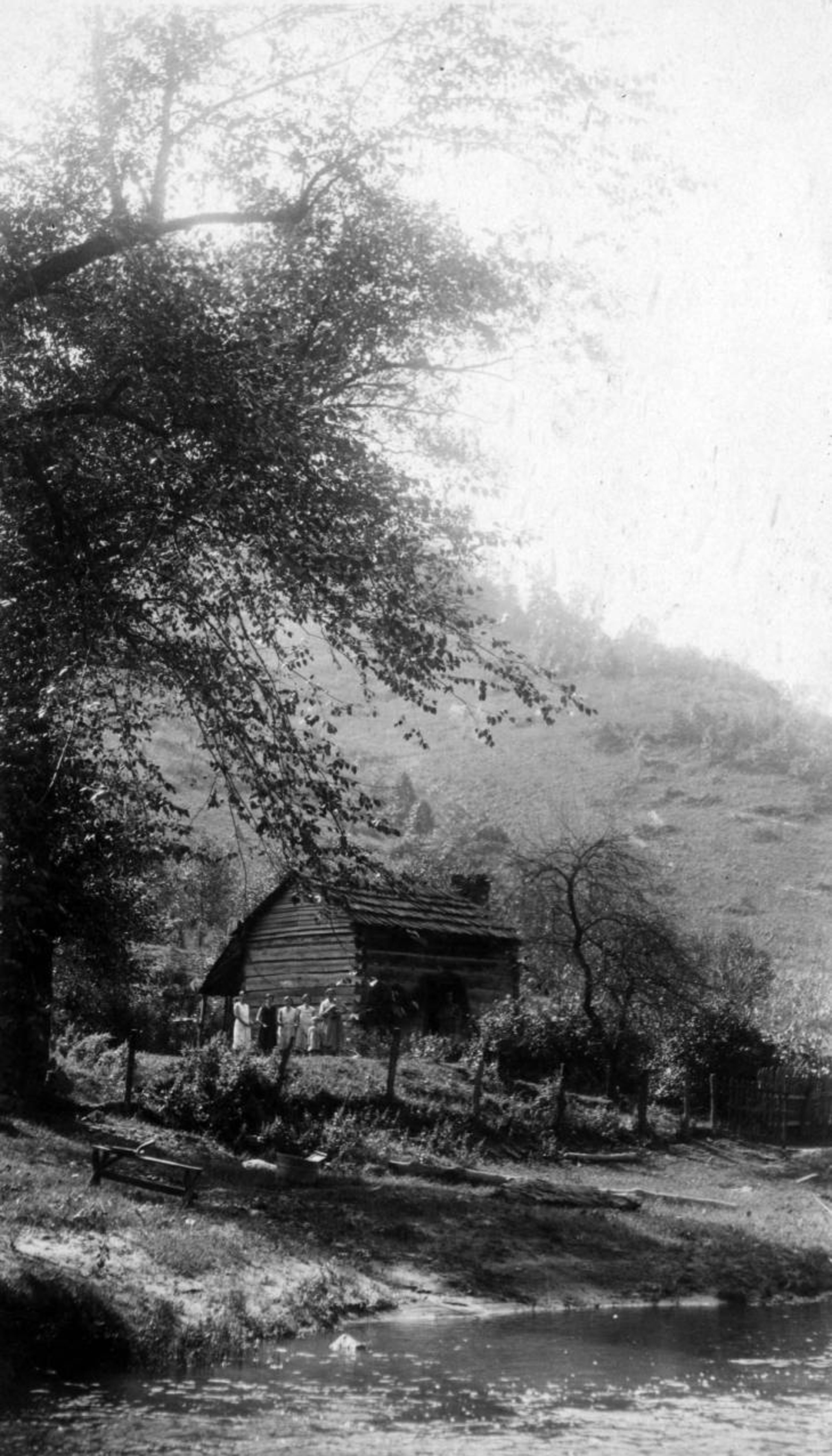 A family stands next to a log cabin, situated near a stream, located in the Georgia mountains circa the 1930s.