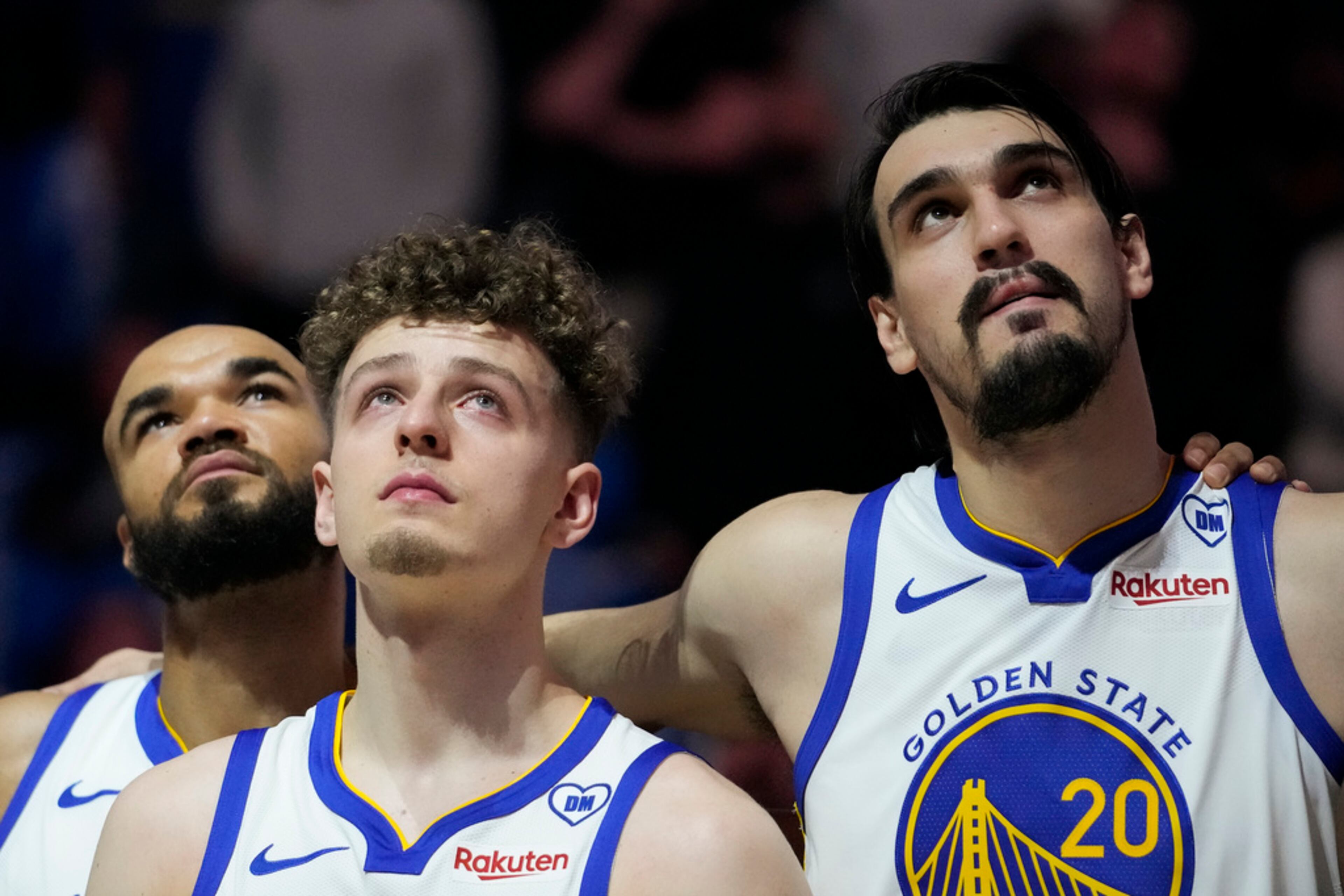 Golden State Warriors' Jerome Robinson, left to right, Brandin Podziemski and Dario Saric watch a video tribute for late assistant coach Dejan Milojevic, who died Jan. 17 after suffering a heart attack, before an NBA basketball game against the Atlanta Hawks, Wednesday, Jan. 24, 2024, in San Francisco. (AP Photo/Godofredo A. Vásquez)