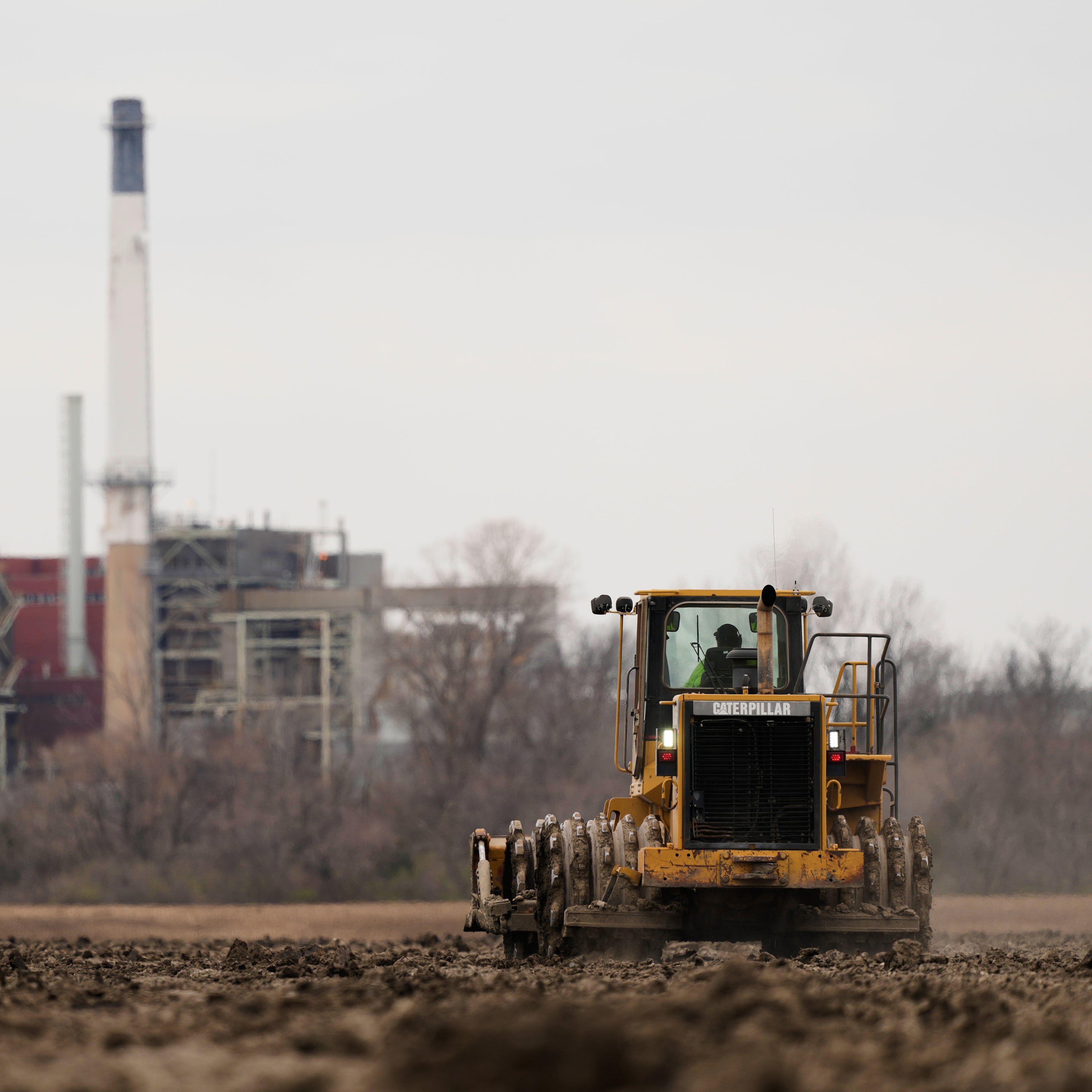 A worker prepares a plot of land for an AI data center, with a retired power plant being refurbished to provide electricity for the facility in the distance, on Tuesday, March 24, 2026, in Independence, Mo. (Charlie Riedel/AP)