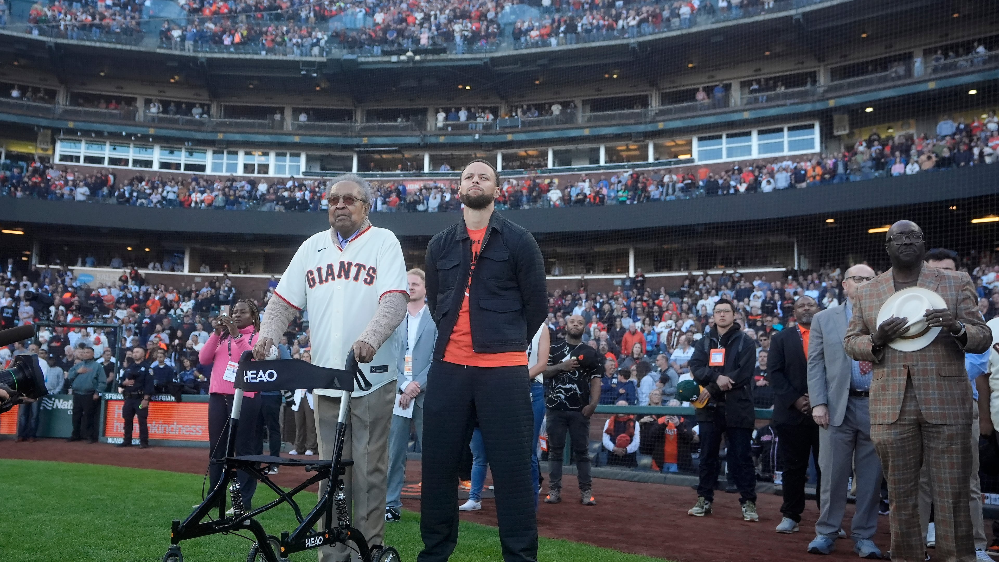 FILE - Dr. Clarence B. Jones, left, a former speech writer for Martin Luther King Jr., stands next to Golden State Warriors basketball player Stephen Curry, front right, during the playing of Lift Every Voice and Sing before a baseball game between the San Francisco Giants and the New York Yankees in San Francisco, May 31, 2024. (AP Photo/Jeff Chiu, File)