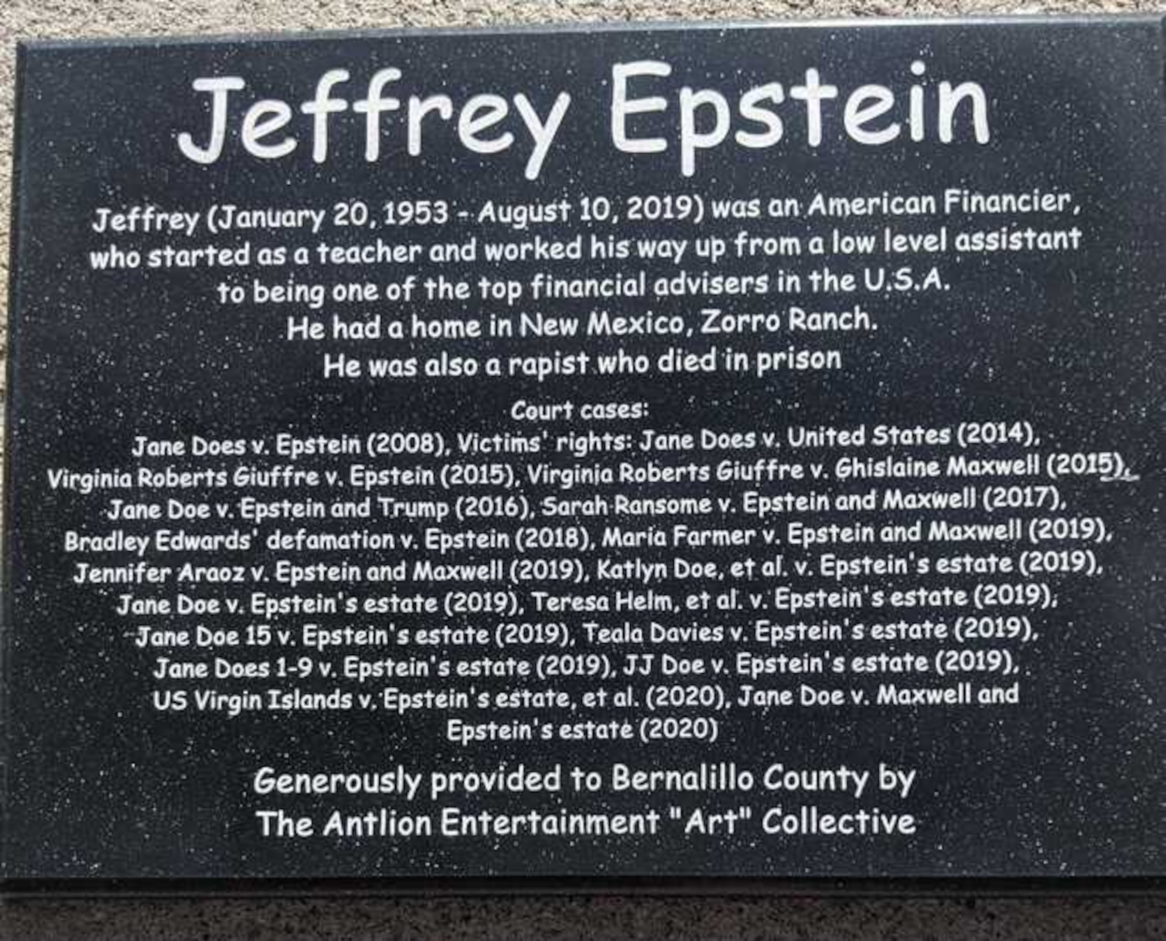 Below the makeshift statue of Epstein was a plaque that read in part: "He had a home in New Mexico, Zorro Ranch. He was also a rapist who died in prison," followed by a list of 18 court cases involving Epstein dating back to 2008. Ghislaine Maxwell's name also appears five times as a defendant.