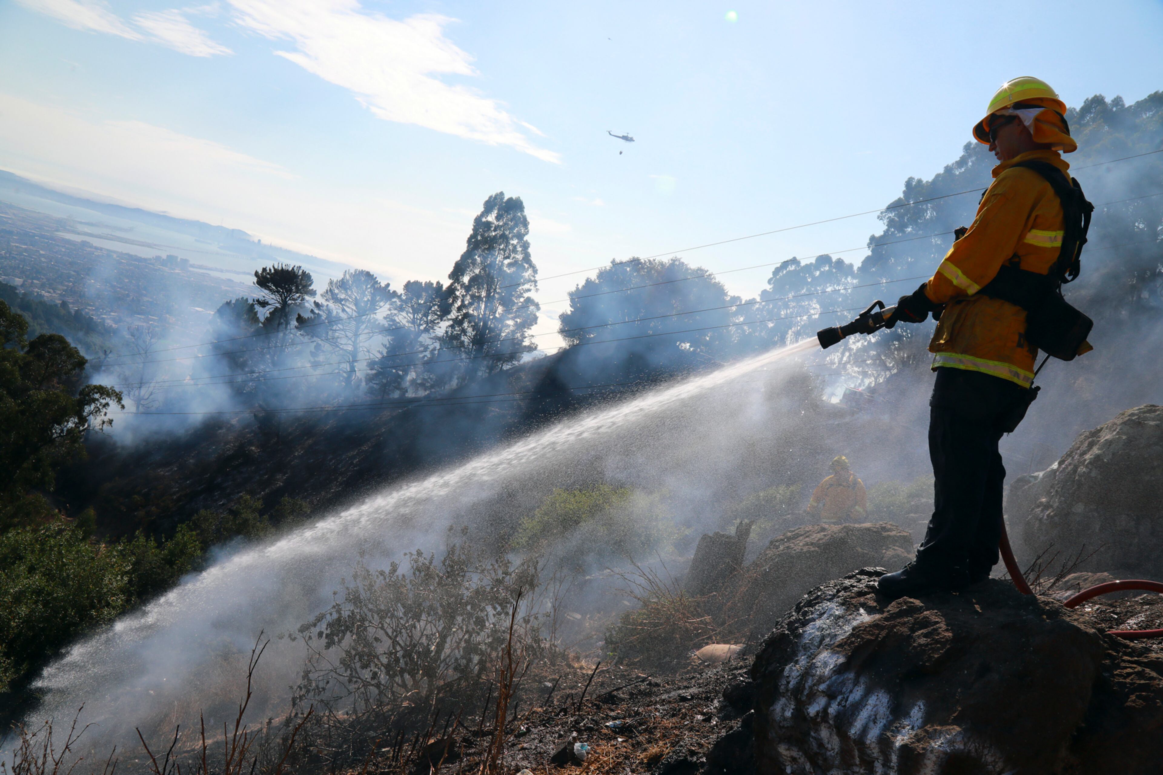 A firefighter doses a hotspot from a brush fire in the Oakland Hills near the University of California, Berkeley, campus in Oakland, Calif., Aug. 2, 2017. (Jim Wilson/The New York Times)