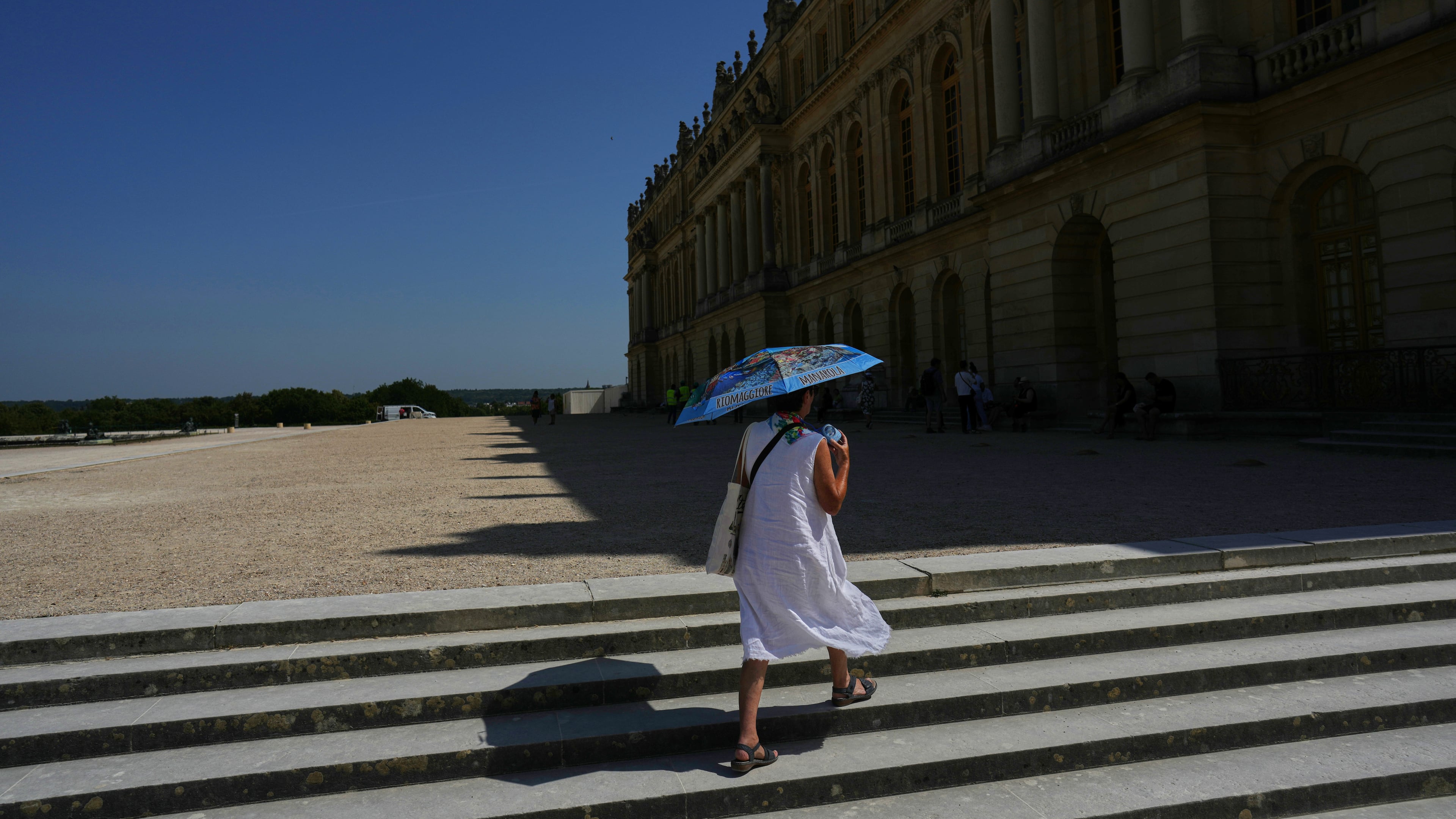 A woman shields herself from the sun with an umbrella as she walks in the garden of the Palace of Versailles, outside Paris, Monday, June 22, 2026. (AP Photo/Thibault Camus)