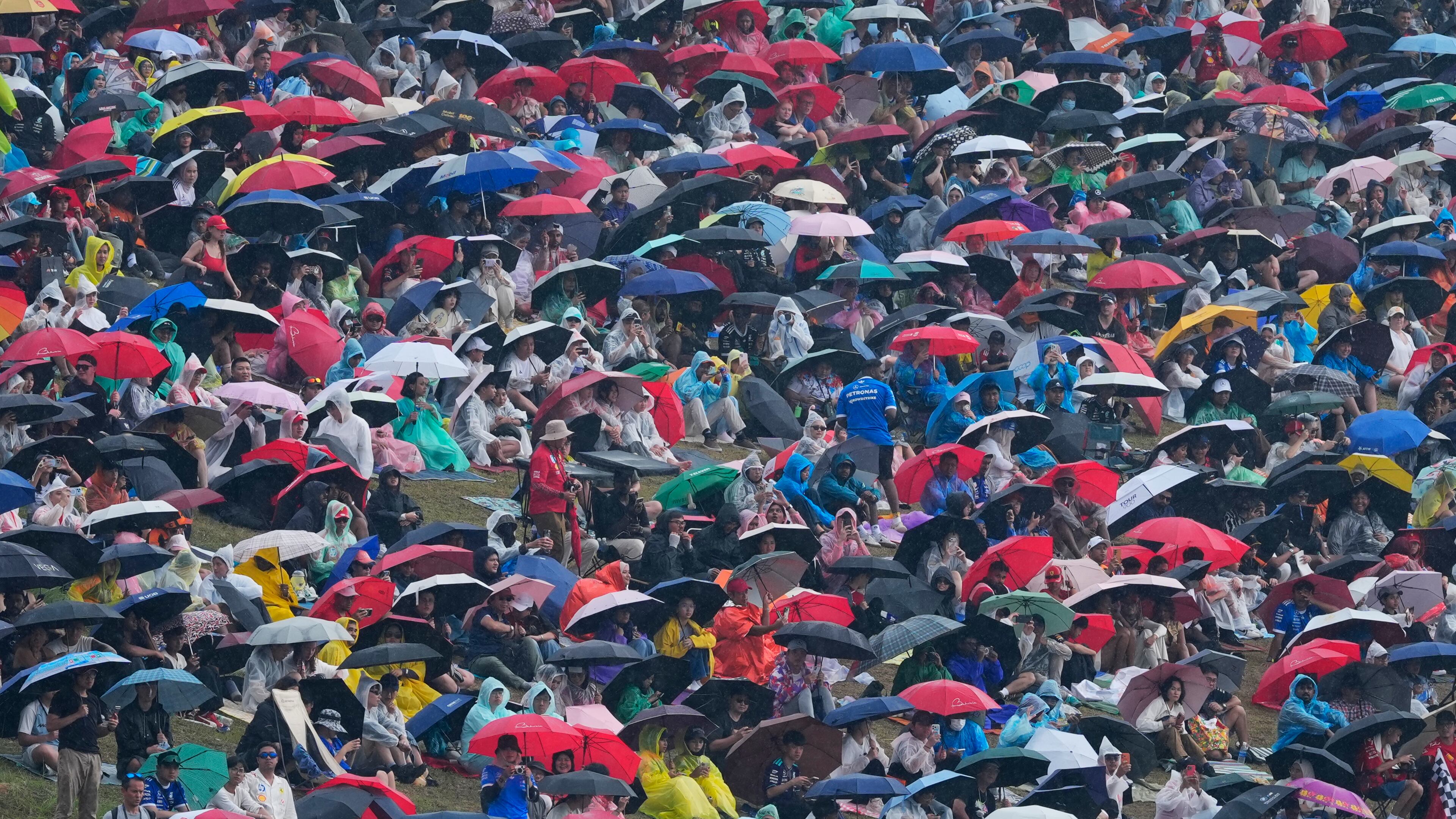 Spectators with umbrella and rain covers gather on a hillside to watch the Bahrain Grand Prix in Sepang, Malaysia, Sunday, Oct. 4, 2026. (AP Photo/Vincent Thian)