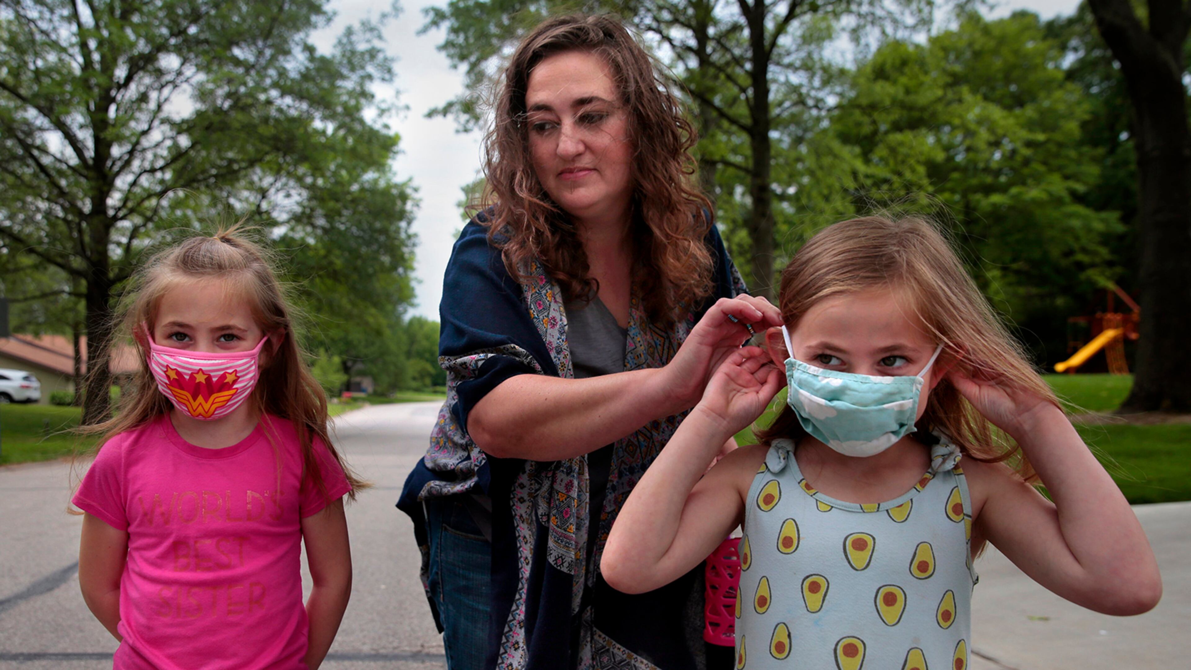 Jenny Berla helps her twins Isla, left, and Elodie with their masks as they approach their sister's school to pick her up after class on Wednesday, May 19, 2021. Berla, who is planning to send the girls to kindergarten this fall, is concerned that dropping mask mandates before young children are eligible for vaccinations leave them open to risk. (Robert Cohen/St. Louis Post-Dispatch/TNS)