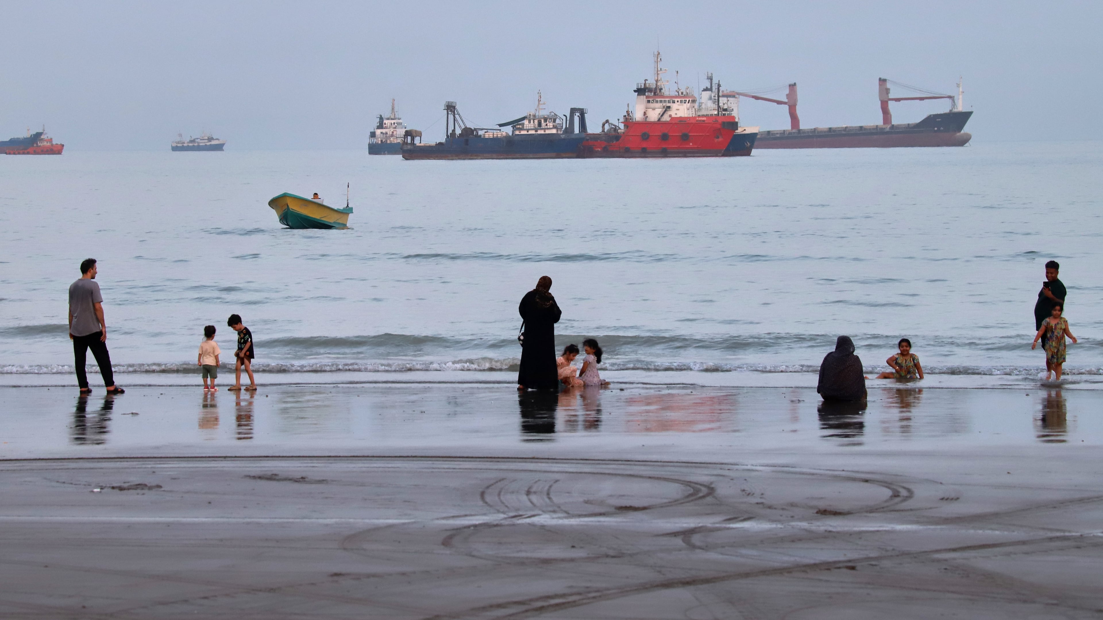 People spend time at a beach as commercial vessels are anchored in the Strait of Hormuz off Bandar Abbas, Iran, Wednesday, Aug. 5, 2026. (Amirhosein Khorgooi/ISNA via AP)