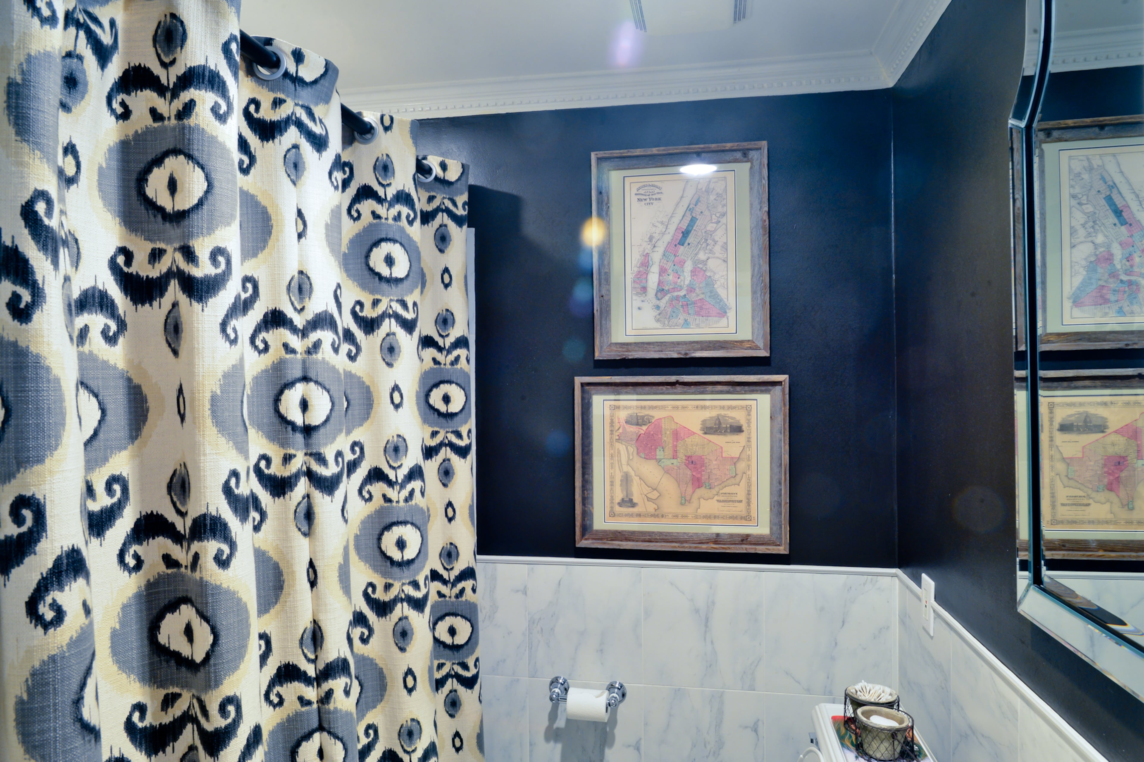 The guest bathroom has a dark painted wall and white marble countertops. The couple found two vintage maps - one of New York and one of Washington D.C. - at Scott Antique Markets and had them framed at Hobby Lobby.