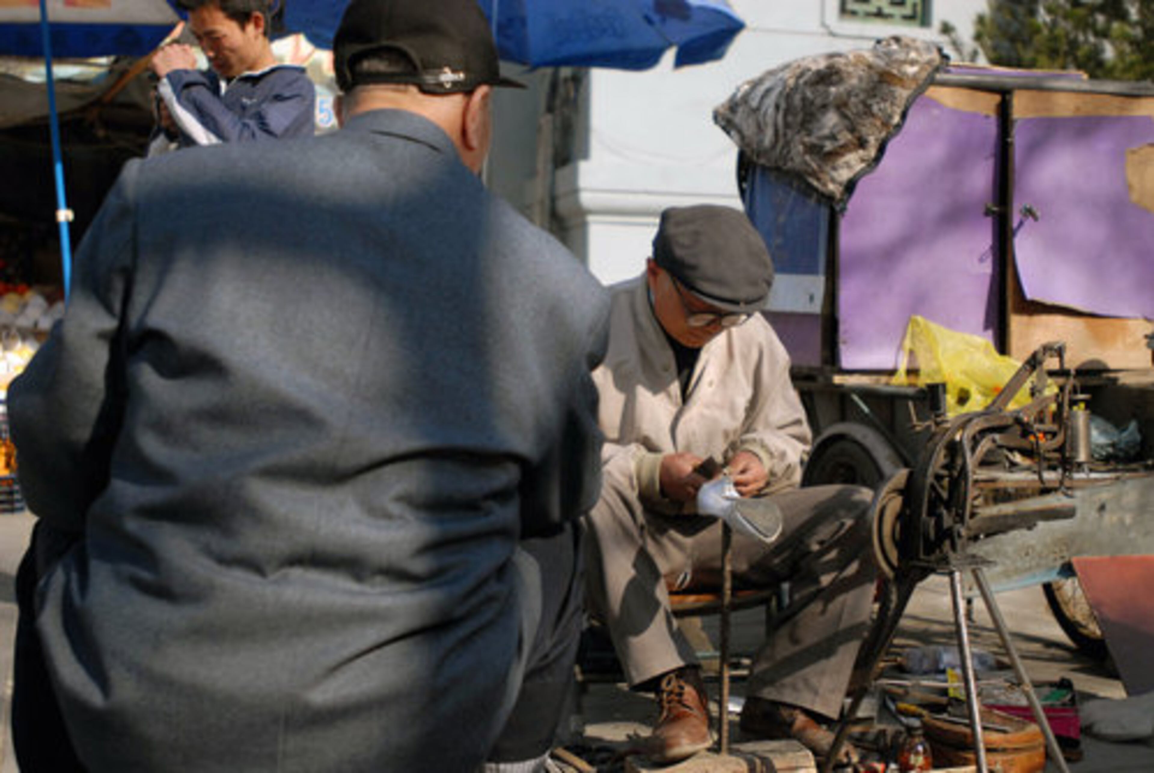 A cobbler repairs shoes in a traditional Beijing neighborhood where commerce often happens outside.