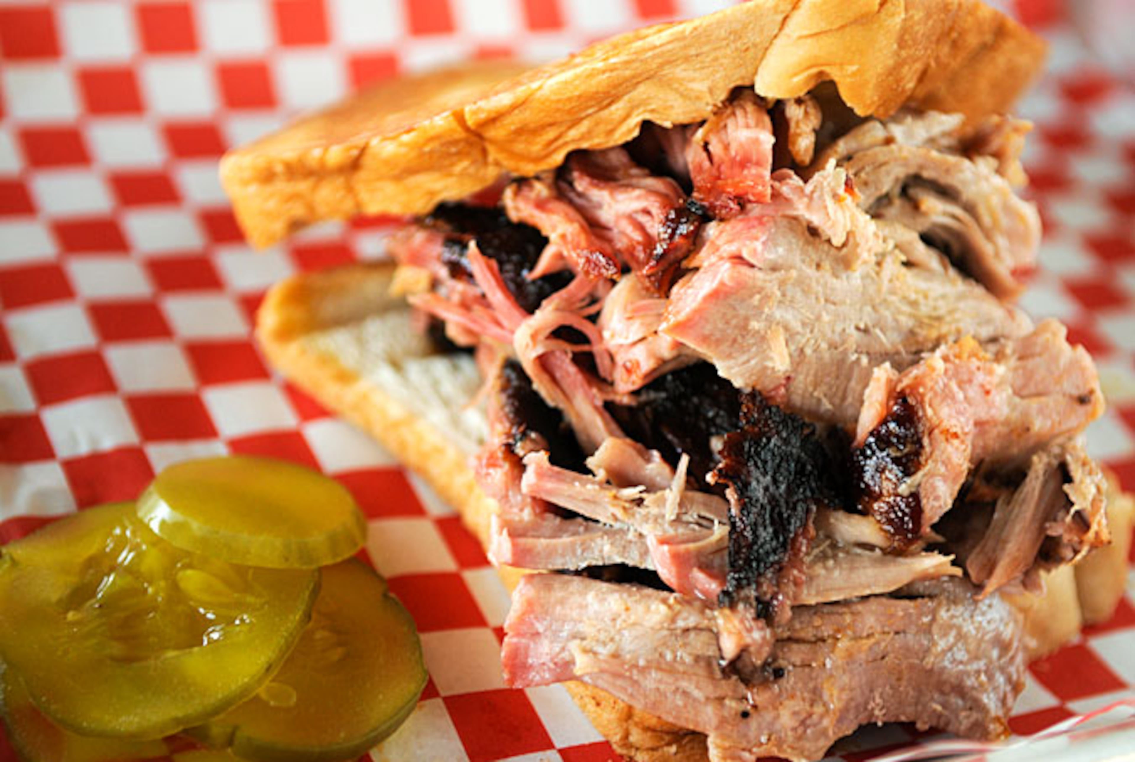 Shreds of tender pork are piled high on thick slices of Texas toast, accompanied by a few slices of dill pickles at Community BBQ. (Courtesy of Becky Stein)
