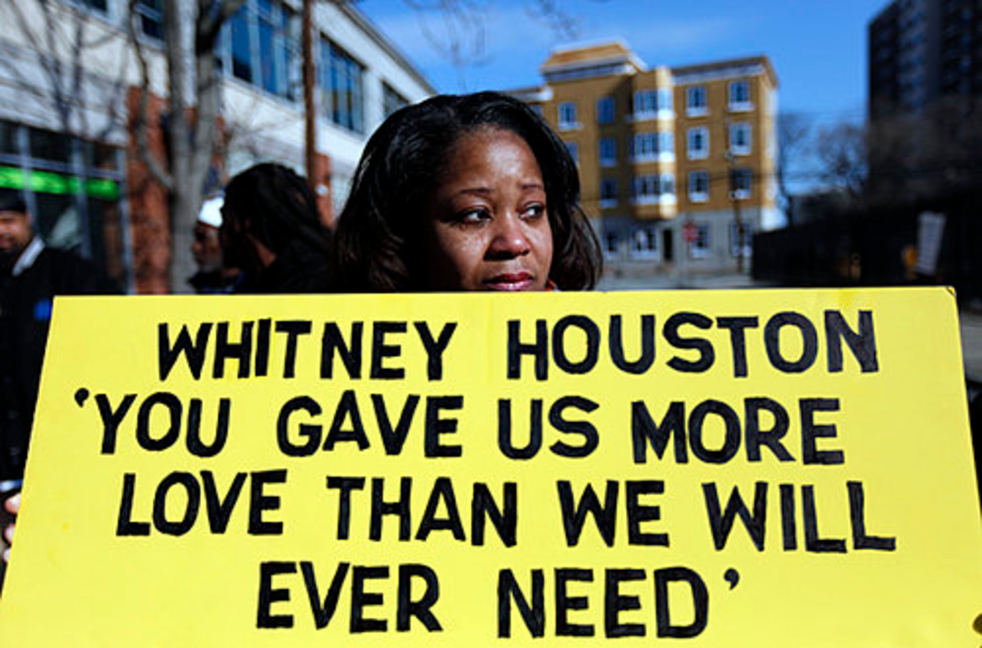 Renee Taylor, of Baltimore, Md., stands with a sign a few blocks from the New Hope Baptist Church before the funeral of Whitney Houston in Newark, N.J., Saturday, Feb. 18, 2012.