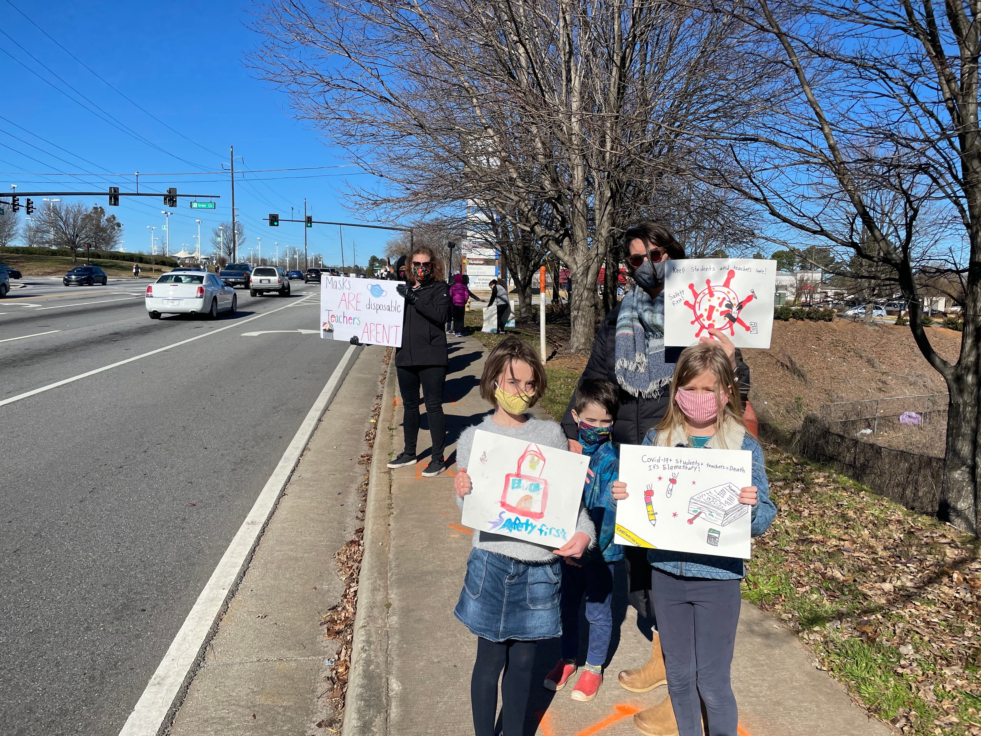 Community members in DeKalb held signs on Tuesday to protest against the reopening of DeKalb County schools.
