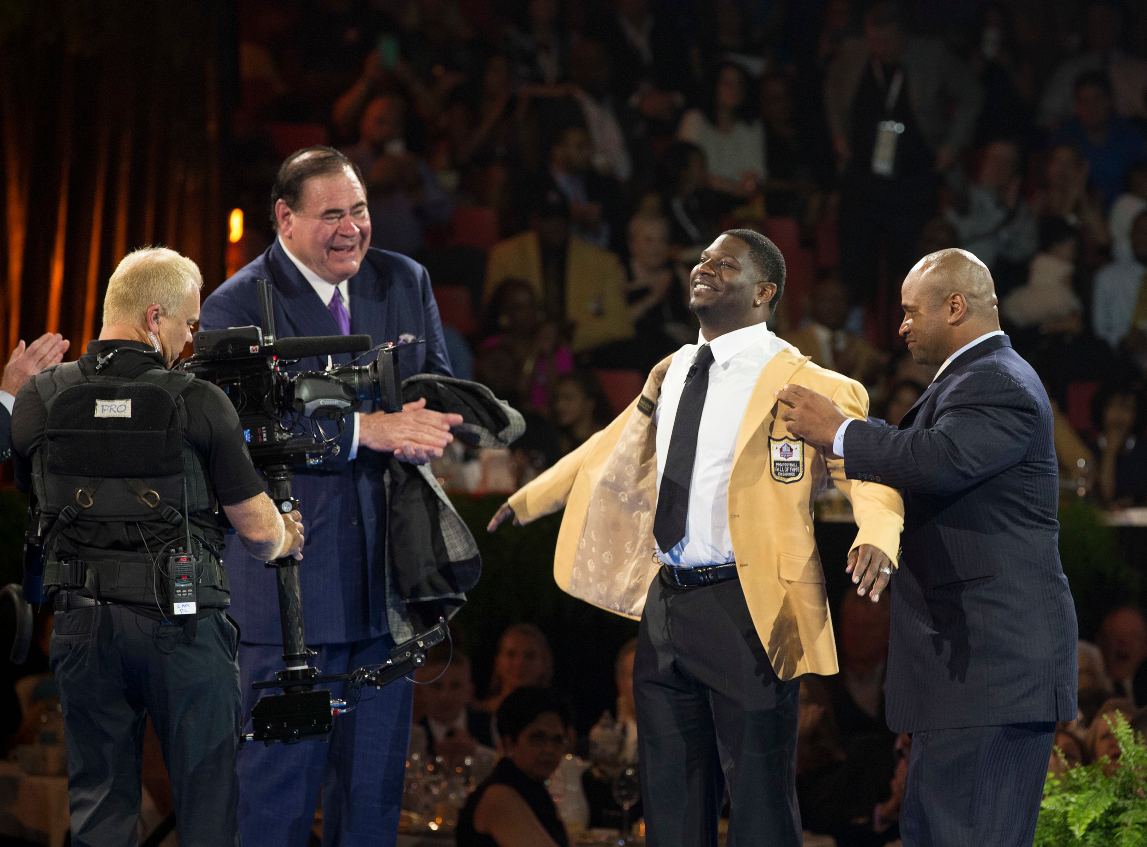 David Baker, president of the Pro Football Hall of Fame, applauds as LaDainian Tomlinson receives his gold jacket from his presenter, Lorenzo Neal, at the Pro Football Hall of Fame enshrinees' dinner, Friday, Aug. 4, 2017, in Canton, Ohio. (Bob Rossiter/The Canton Repository via AP)
