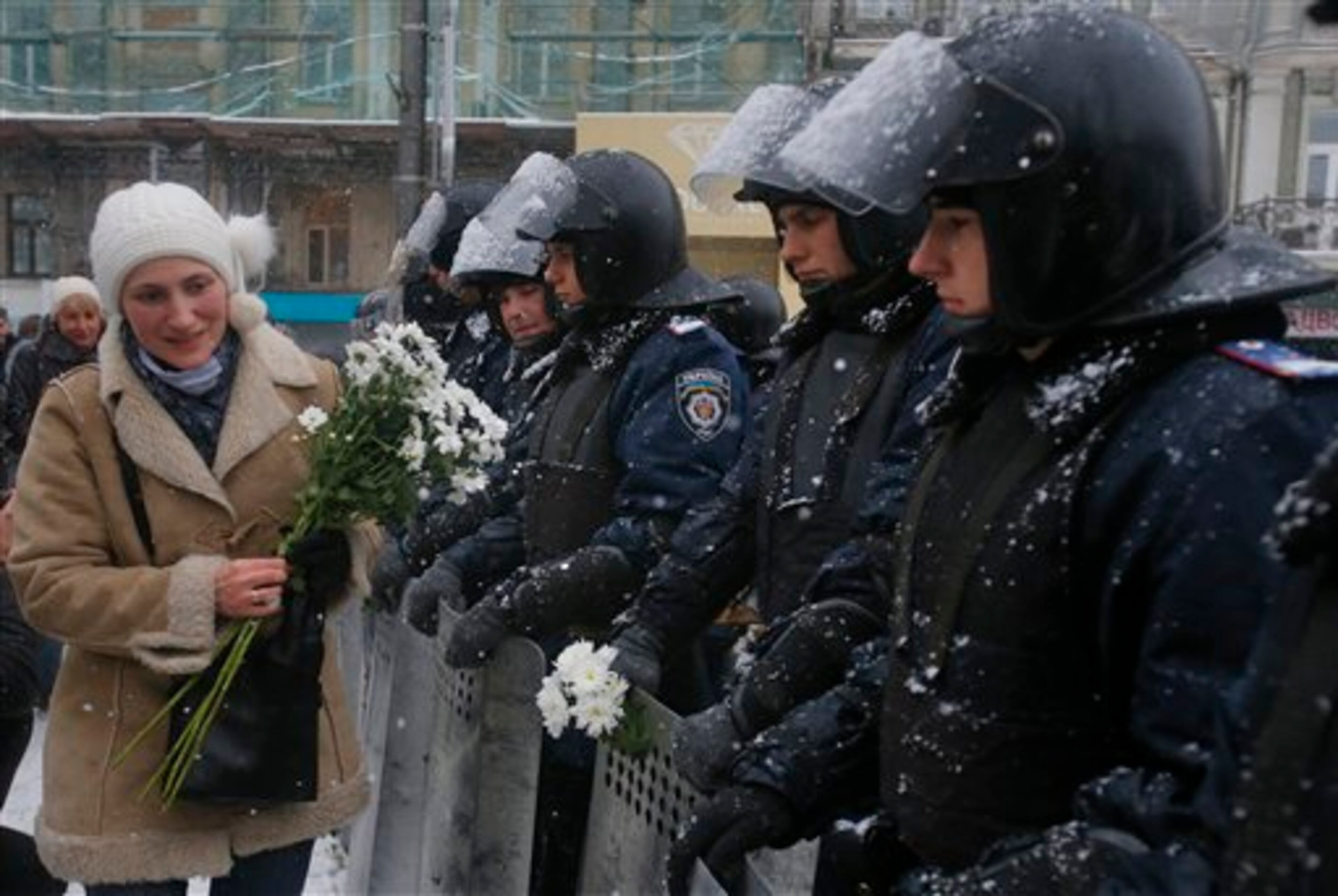 A woman gives flowers to Ukrainian riot police as they block the road next to Pro-European Union activists gathered on the Independence Square in Kiev, Ukraine, Monday, Dec. 9, 2013. The policemen, wearing helmets and holding shields, formed a chain across Kiev�s main street outside the city building. Organizers called on protesters to vacate the city hall and the other building which the opposition had used as its headquarters. (AP Photo/Sergei Grits)
