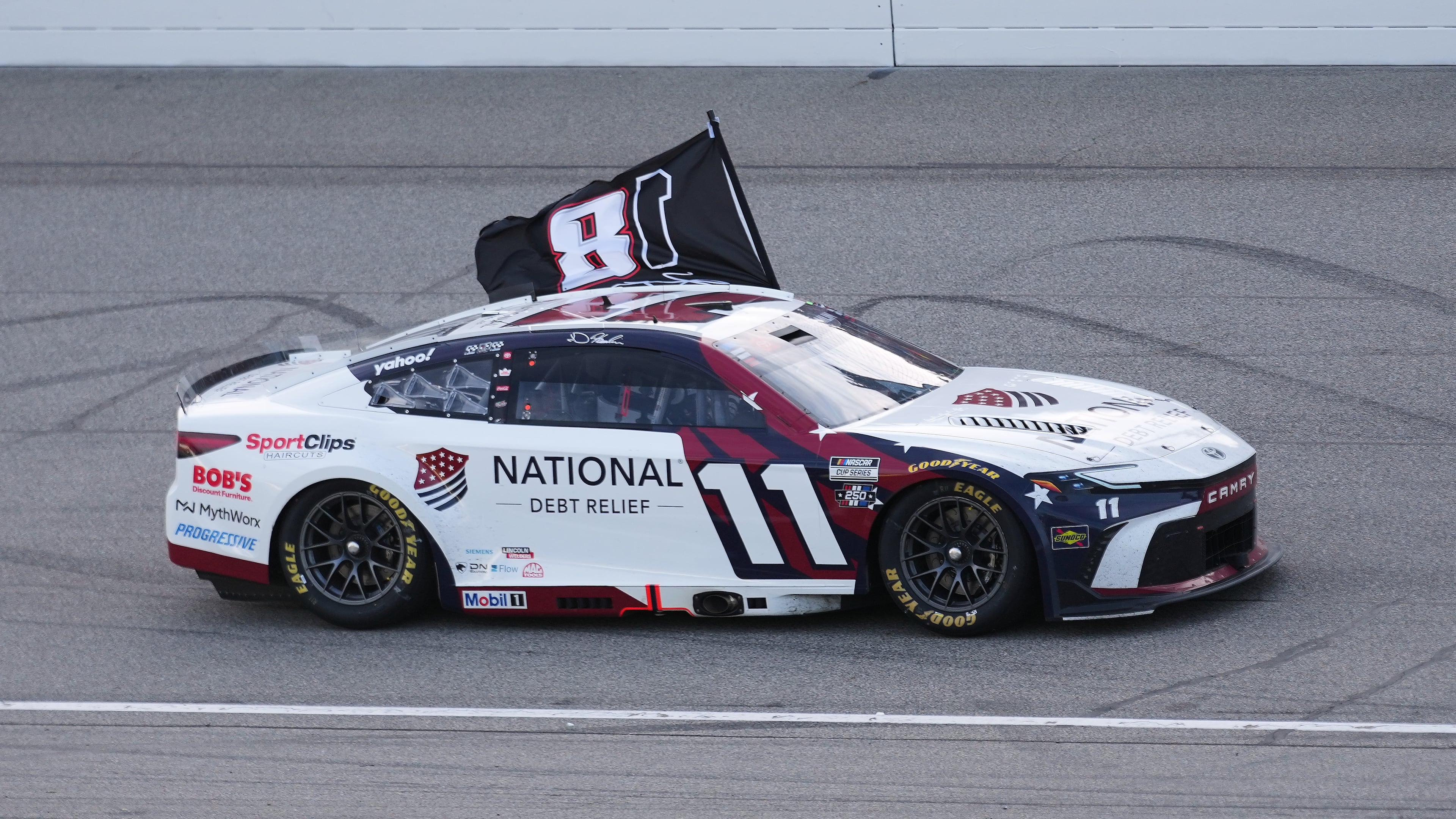 Denny Hamlin celebrates winning while honoring Kyle Busch with a flag after a NASCAR Cup Series auto race at Michigan International Speedway in Brooklyn, Mich., Sunday, June 7, 2026. (AP Photo/Paul Sancya)