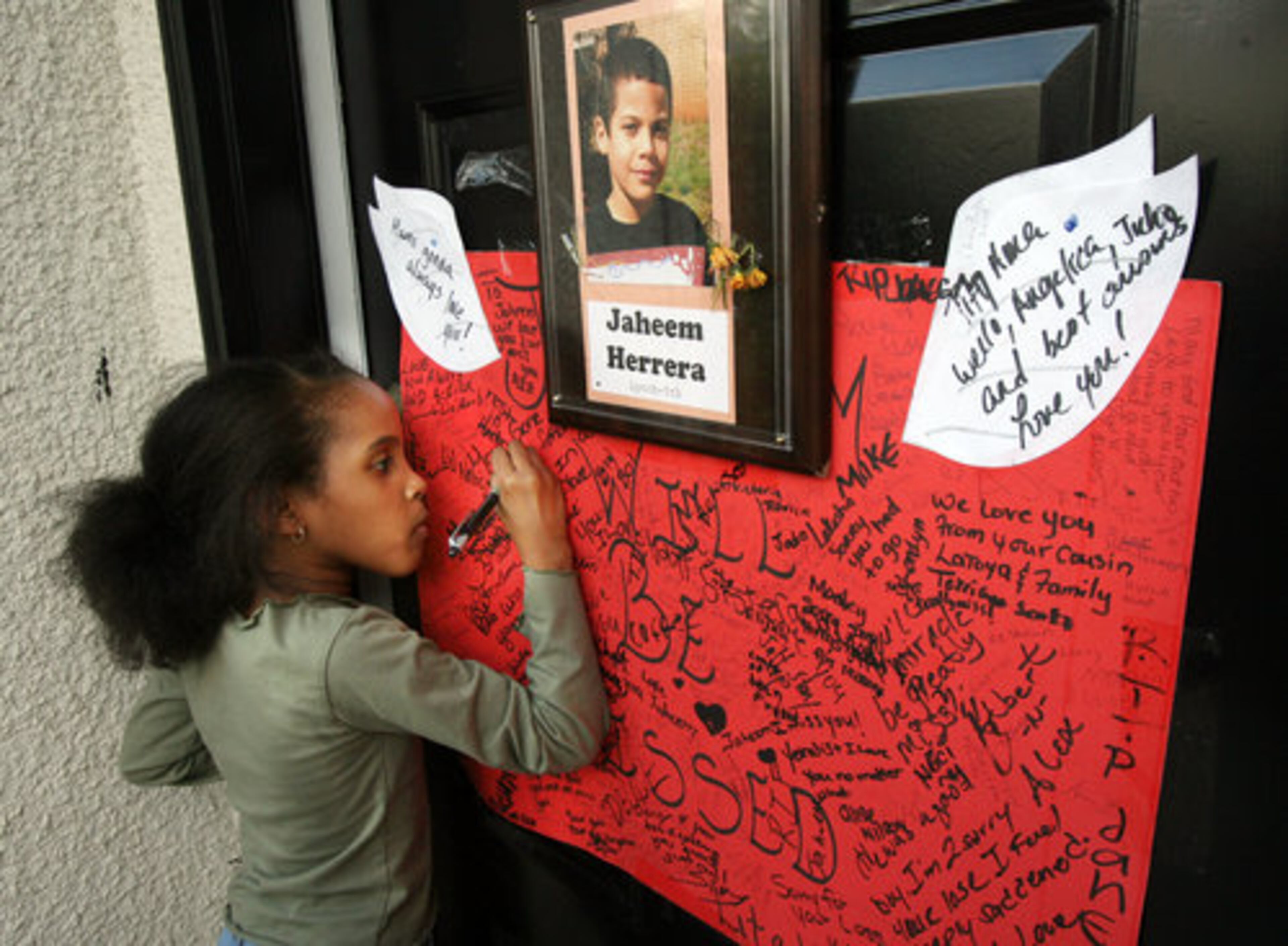 Ny'irah Keene, the sister of Jaheem Herrera, writes "I Love You Jaheem" on a shrine at the family's front door as people began to gather at the boy's DeKalb home. About 60 came to remember the fifth-grader who committed suicide last week. The 11-year-old boy hanged himself at his home after -- according to his family -- relentless bullying at Dunaire Elementary.