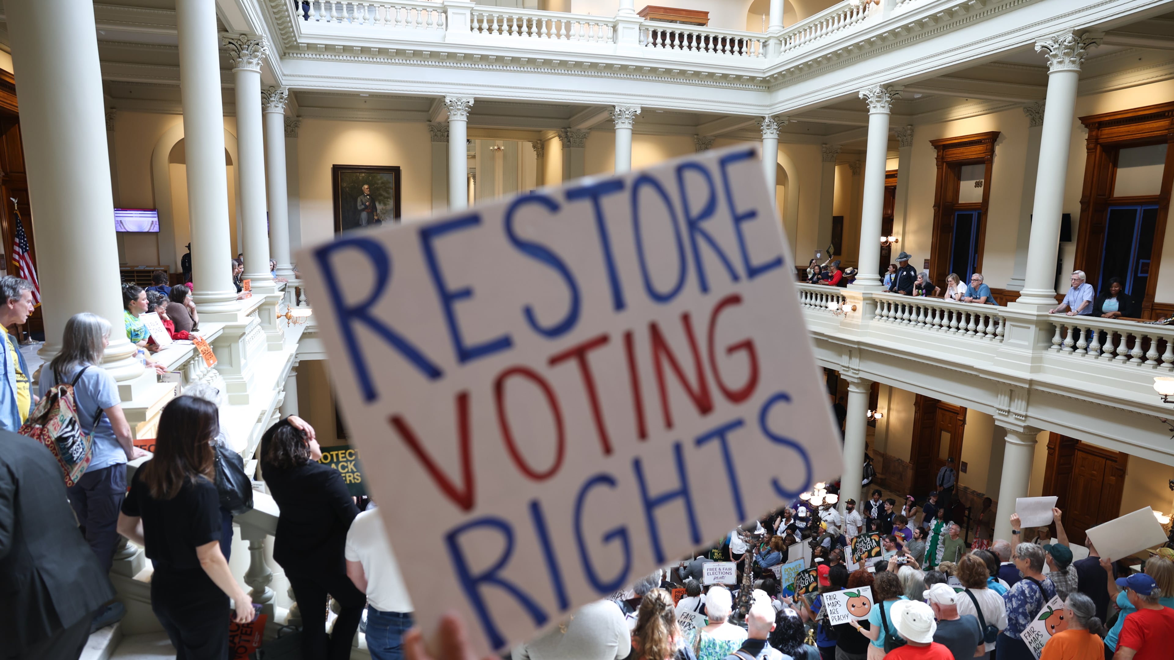 An activist holds a "Restore Voting Rights" sign at a news conference before the state Legislature convenes for a special session at the Capitol on Wednesday. (Arvin Temkar/AJC)