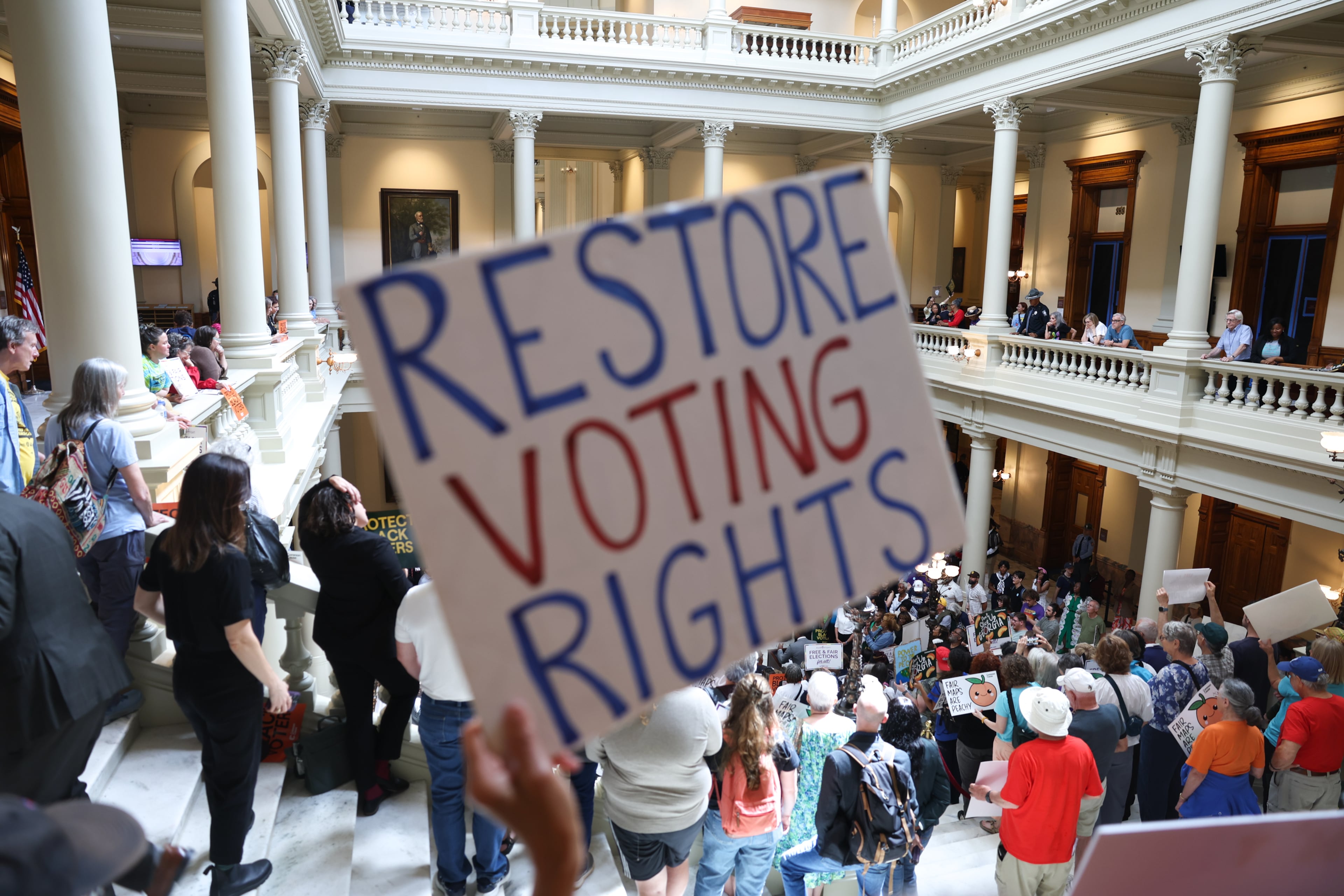 An activist holds a “Restore Voting Rights” sign at a press conference before the state legislature convenes for a special session in Atlanta on June 17, 2026. Georgia Republican leaders later announced that they wouldn’t redraw the state’s political maps during the session. (Arvin Temkar/AJC)