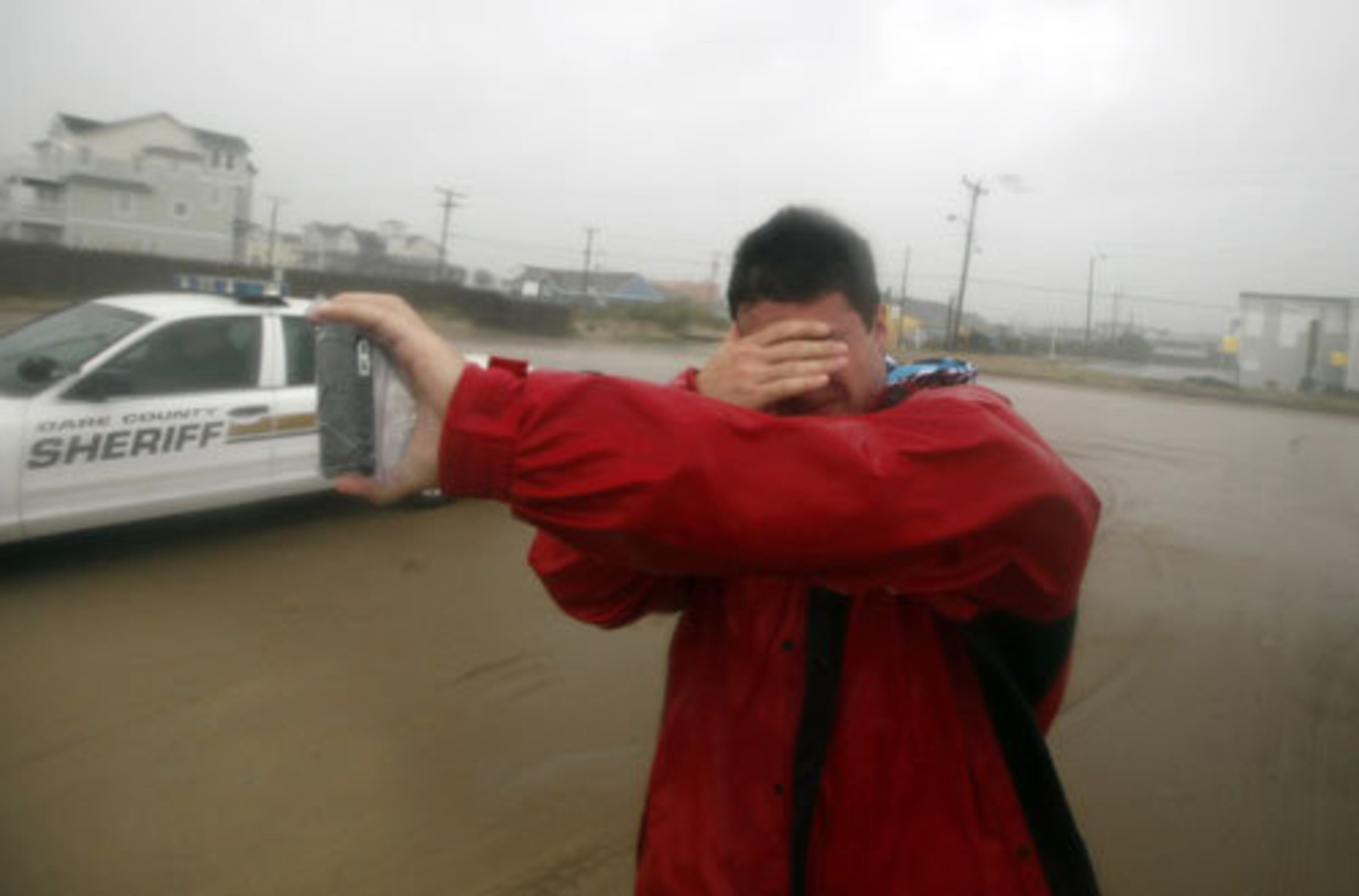 Shielding his eyes from the driving sand, Mike Scruggs takes a photo of the beach at Avalon Pier in Kill Devil Hills, N.C., during Hurricane Irene on Saturday, Aug. 27, 2011.