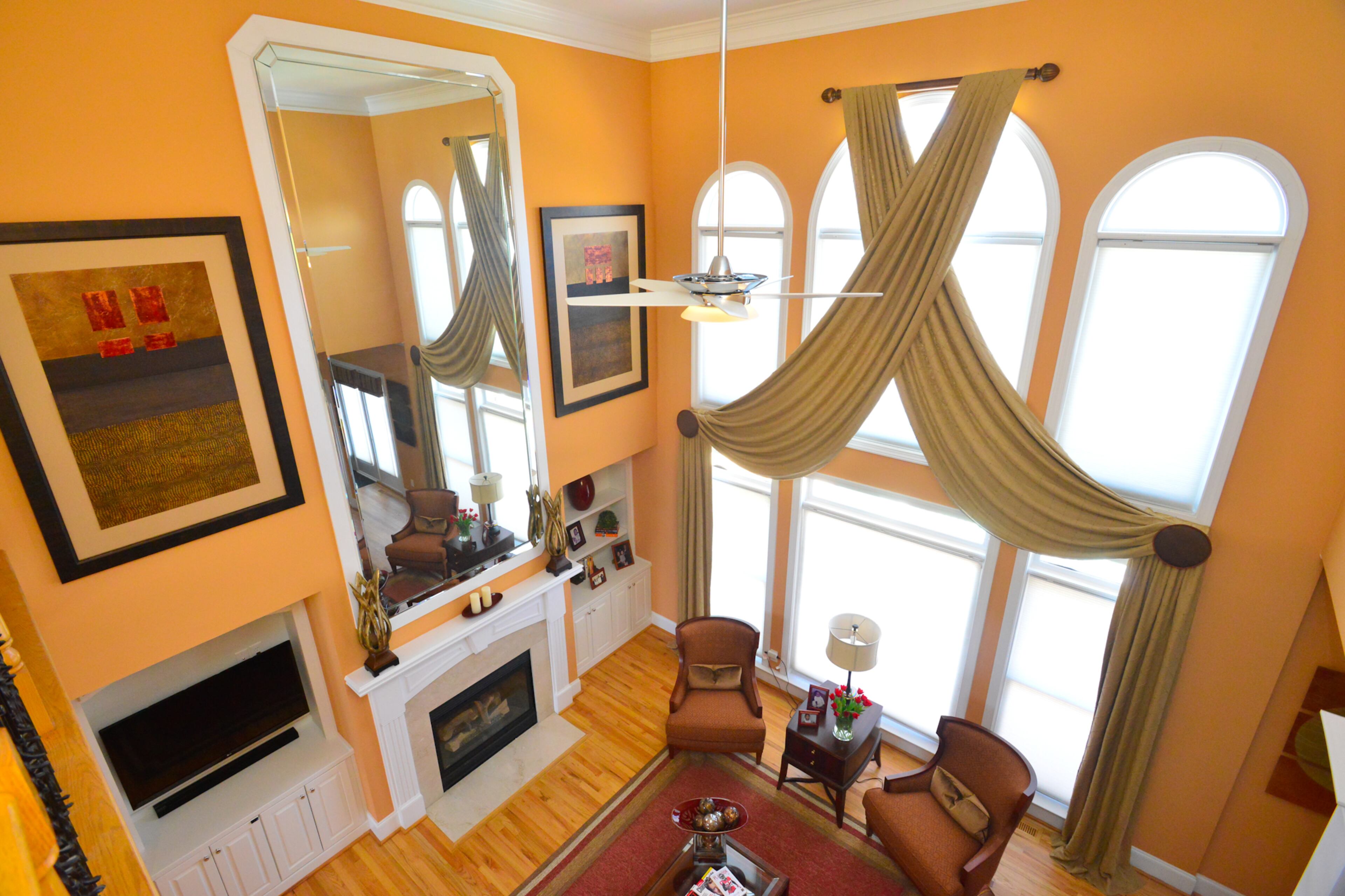 The dramatic window treatments in the living room were designed by designed by Barbara Elliott and Jennifer Ward Woods of Decorating Den Interiors and created by Atlanta's Finest Design, using fabric from Trend. The walls are painted Georgia Peach, and the room includes a custom-made sofa, wing chairs and accent chairs by Taylor King Furniture, two framed textured collages from Kinder Harris and a ceiling fan from Casablanca Fan.