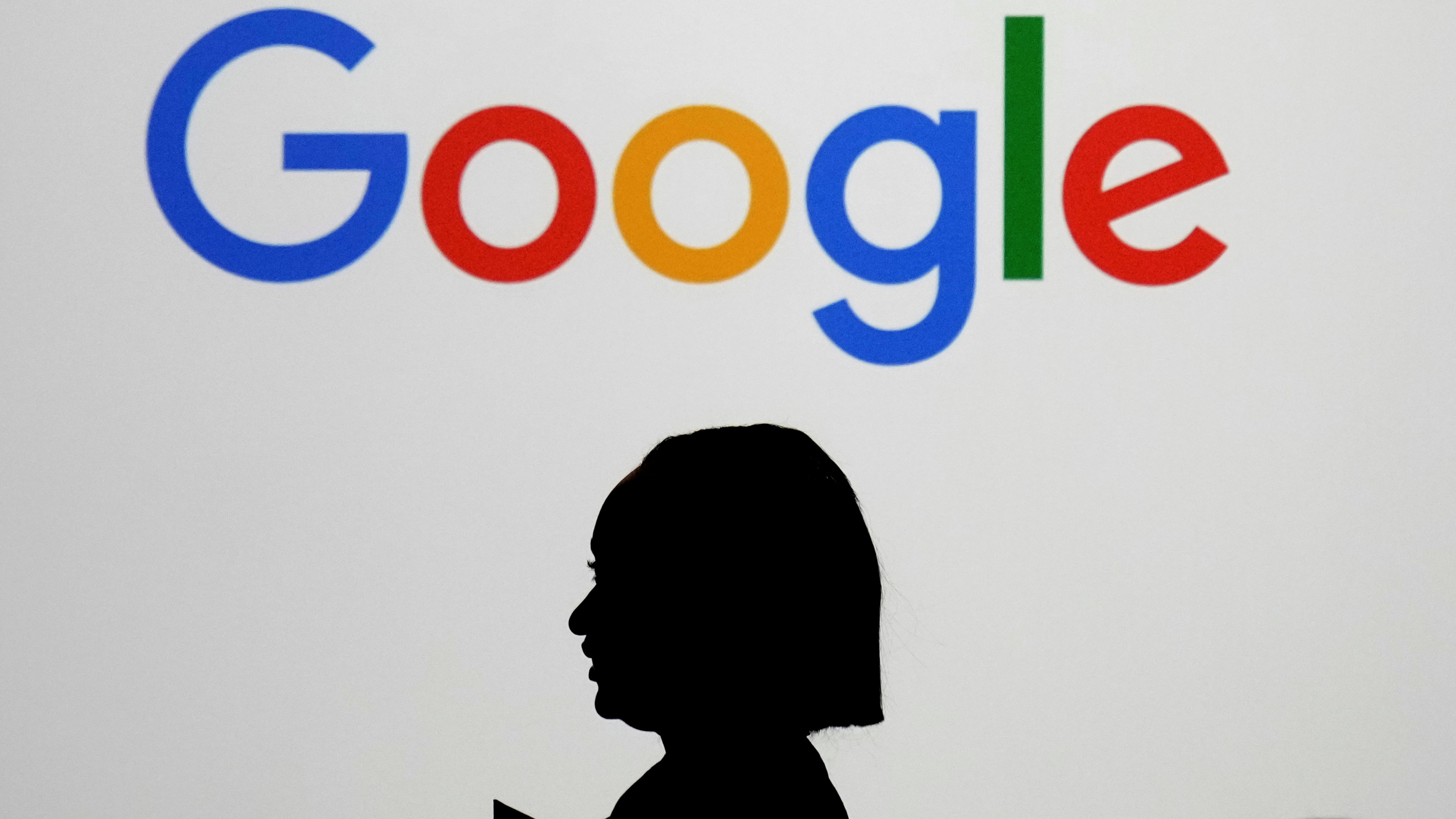 FILE - A woman walks by a giant screen with a logo at an event at the Paris Google Lab on the sidelines of the AI Action Summit in Paris, on Feb. 9, 2025. (AP Photo/Thibault Camus,File)