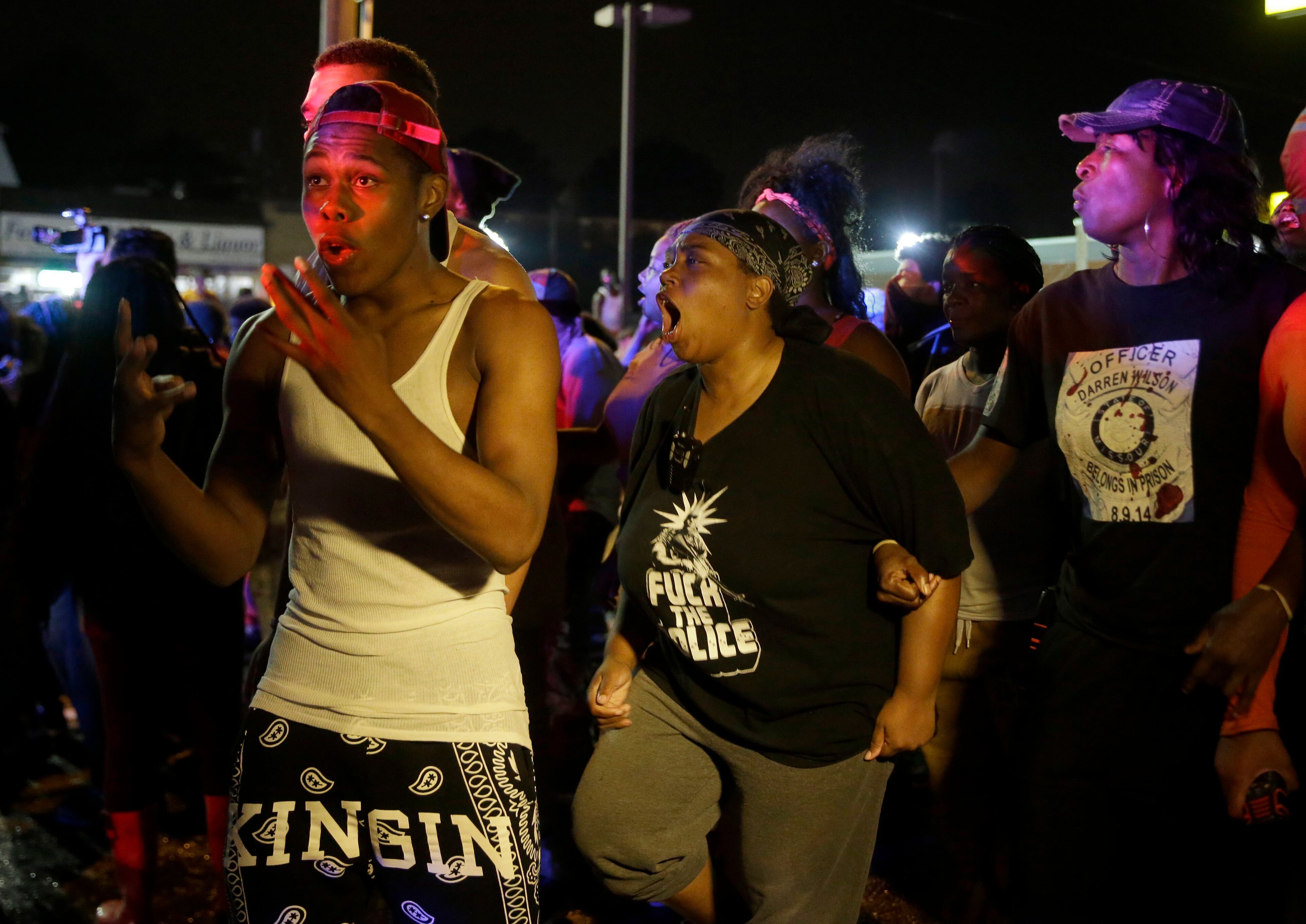 Protesters yell at police, Sunday, Aug. 9, 2015, in Ferguson, Mo., before shots were fired near the protest. The one-year anniversary of Michael Brown's death in Ferguson began with a march in his honor and ended with a protest that was interrupted by gunfire. (AP Photo/Jeff Roberson)