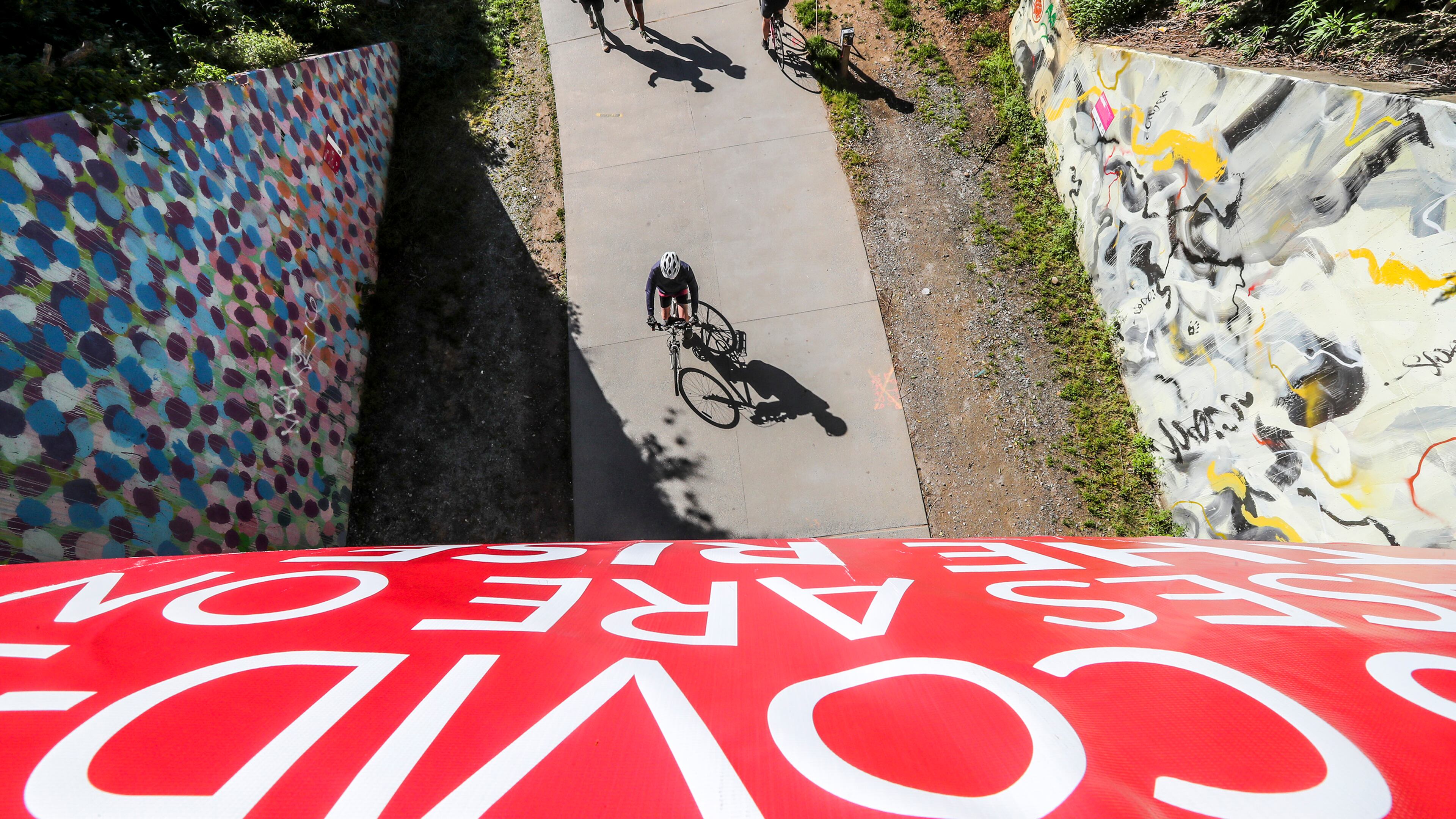 A COVID-19 sign flaps in the wind above people on the Beltline near 10th and Monroe Drive in Atlanta on Friday, May 1, 2020, after Gov. Brian Kemp lifted a shelter-at-home mandate for most Georgians on Thursday, ending the state’s most ambitious attempt to slow the spread of the new coronavirus. JOHN SPINK/JSPINK@AJC.COM