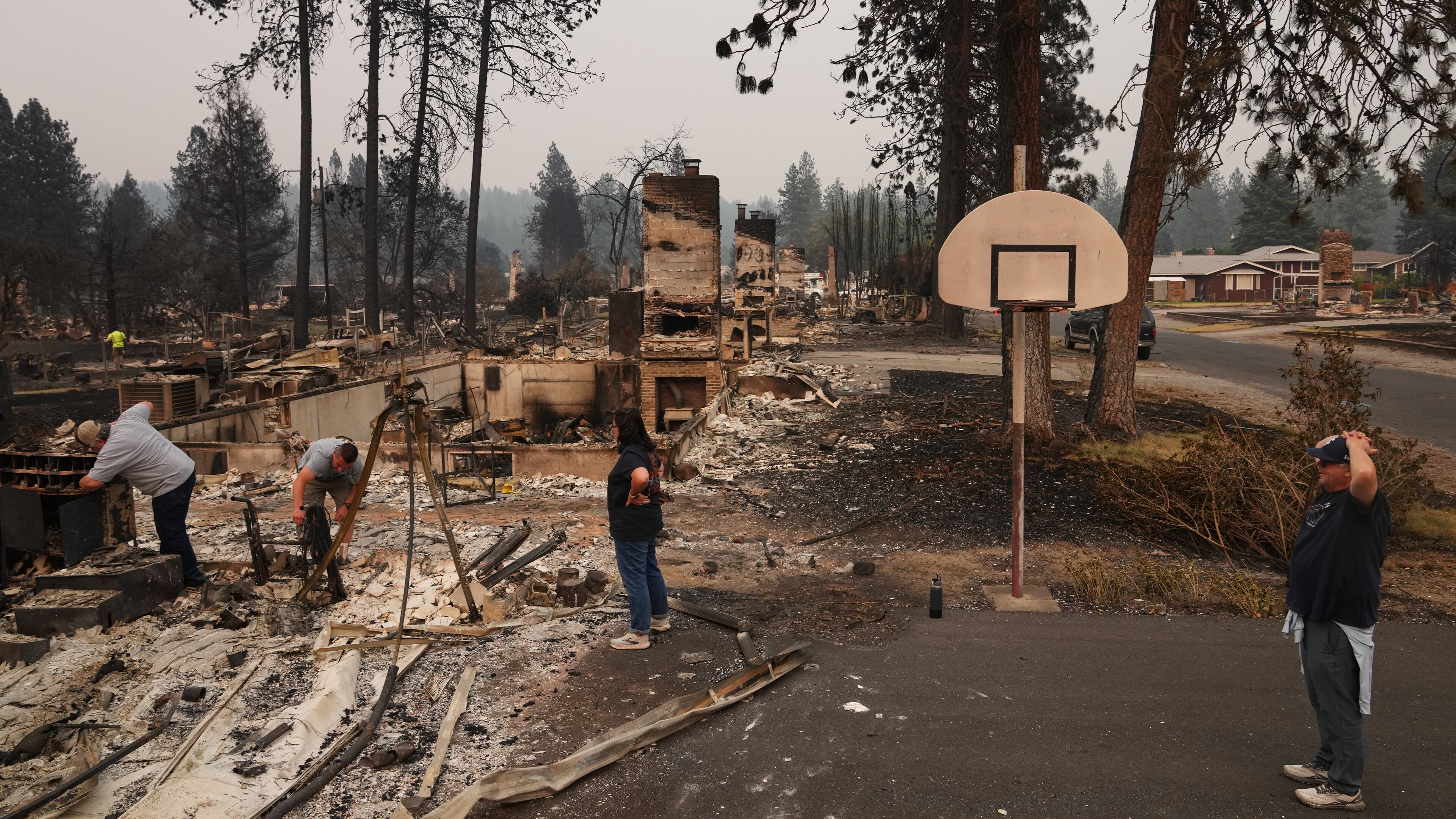 From left, homeowner Al Acosta, his son Louis Acosta, daughter Renee Stewart and son-in-law Jamie Stewart look through the remains of Al's home after a wildfire hit the northern part of Spokane, Wash., Monday, Aug. 3, 2026. (AP Photo/Lindsey Wasson)