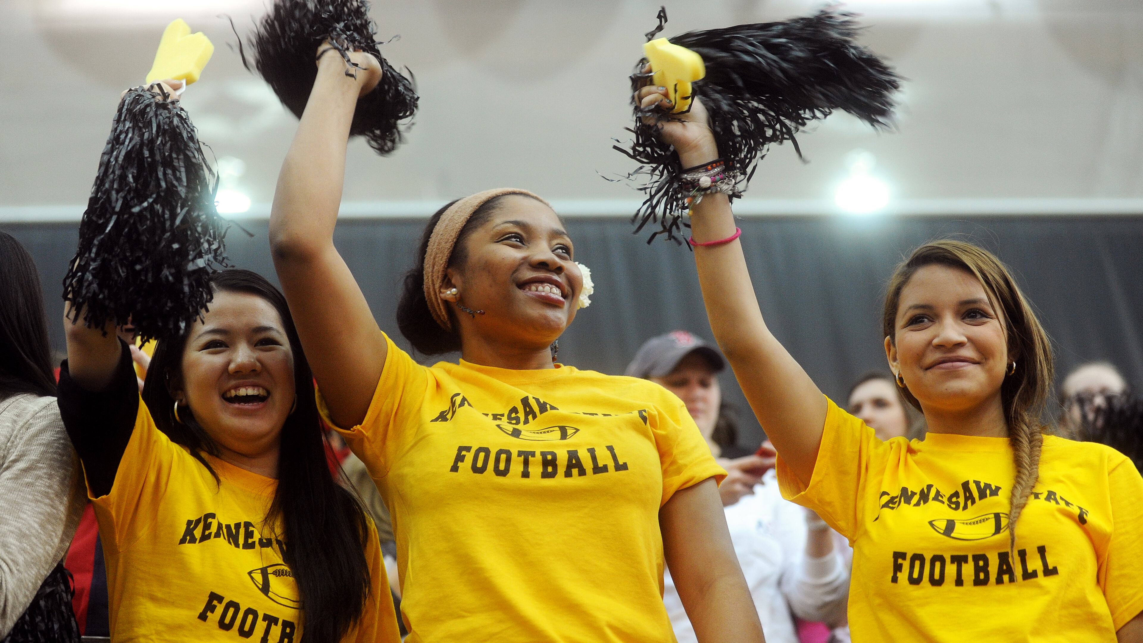 Kennesaw State University students (from left) Nobuko Saito, Chioma Amako and Alejandra Palencia cheer enthusiastically as they attend a news conference held in the school's Convocation Center to announce Fifth Third Bank as a $5 million sponsor of KSU's new football program.