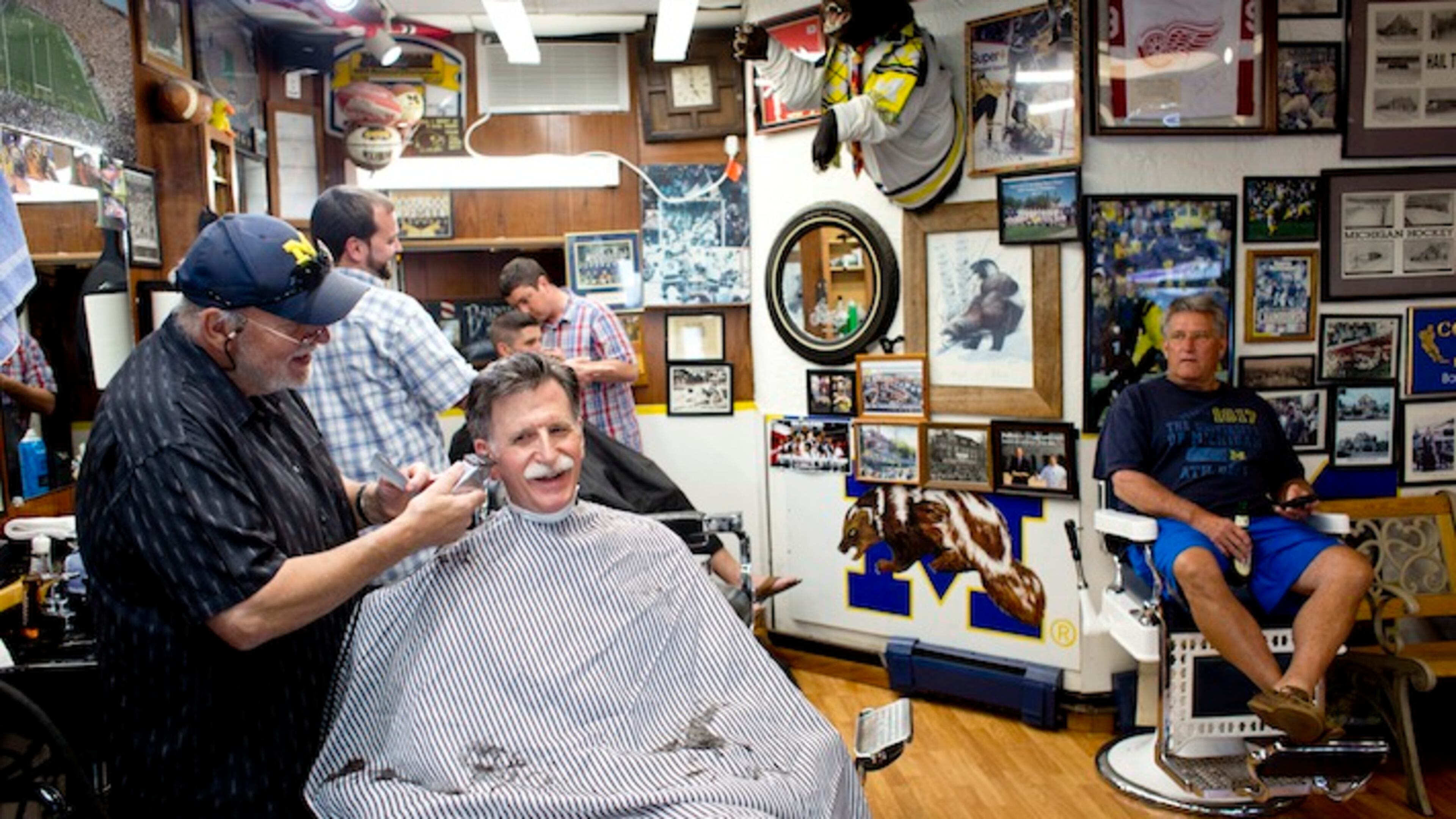 Jerry Erickson gives a haircut at his Coach and Four Barber Shop in Ann Arbor, Mich., July 22, 2015. Jim Harbaugh’s return to the University of Michigan, where he is set for his first home game in charge, has re-energized longtime fans, including those at this barbershop, once a favored haunt of the Wolverines' legendary coach Bo Schembechler. (Laura McDermott/The New York Times)
