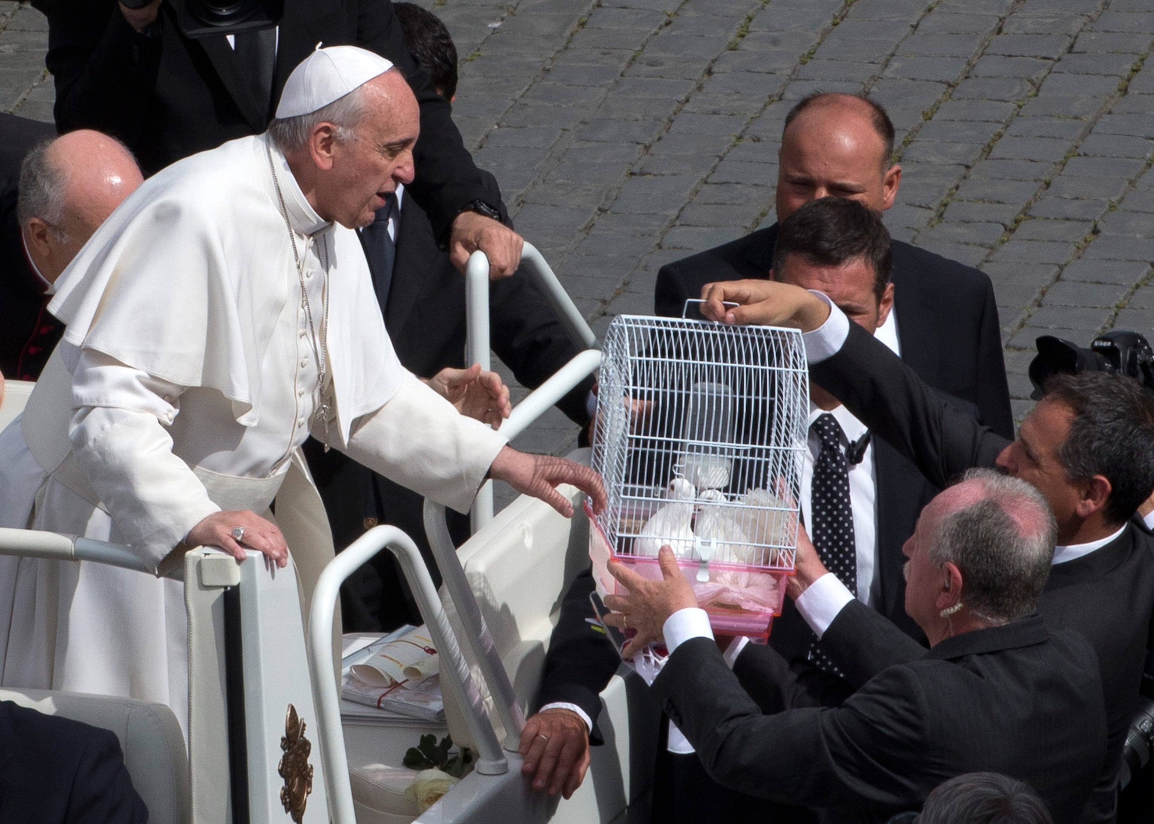 Security personnel hand Pope Francis a cage containing two doves during his weekly general audience in St. Peter Square at the Vatican, Wednesday, May 15, 2013. As Francis toured the square in his open-topped popemobile at his Wednesday audience with the public, someone at the edge of the crowd thrust a white bird cage at him. Looking puzzled, his security detail took the cage, containing a pair of white doves, and handed it to Francis. Without hesitation, the pope opened the cage door, thrust a hand inside and extracted one dove, and with a flick of his hand, sent the bird flying over the square. (AP Photo/Alessandra Tarantino)